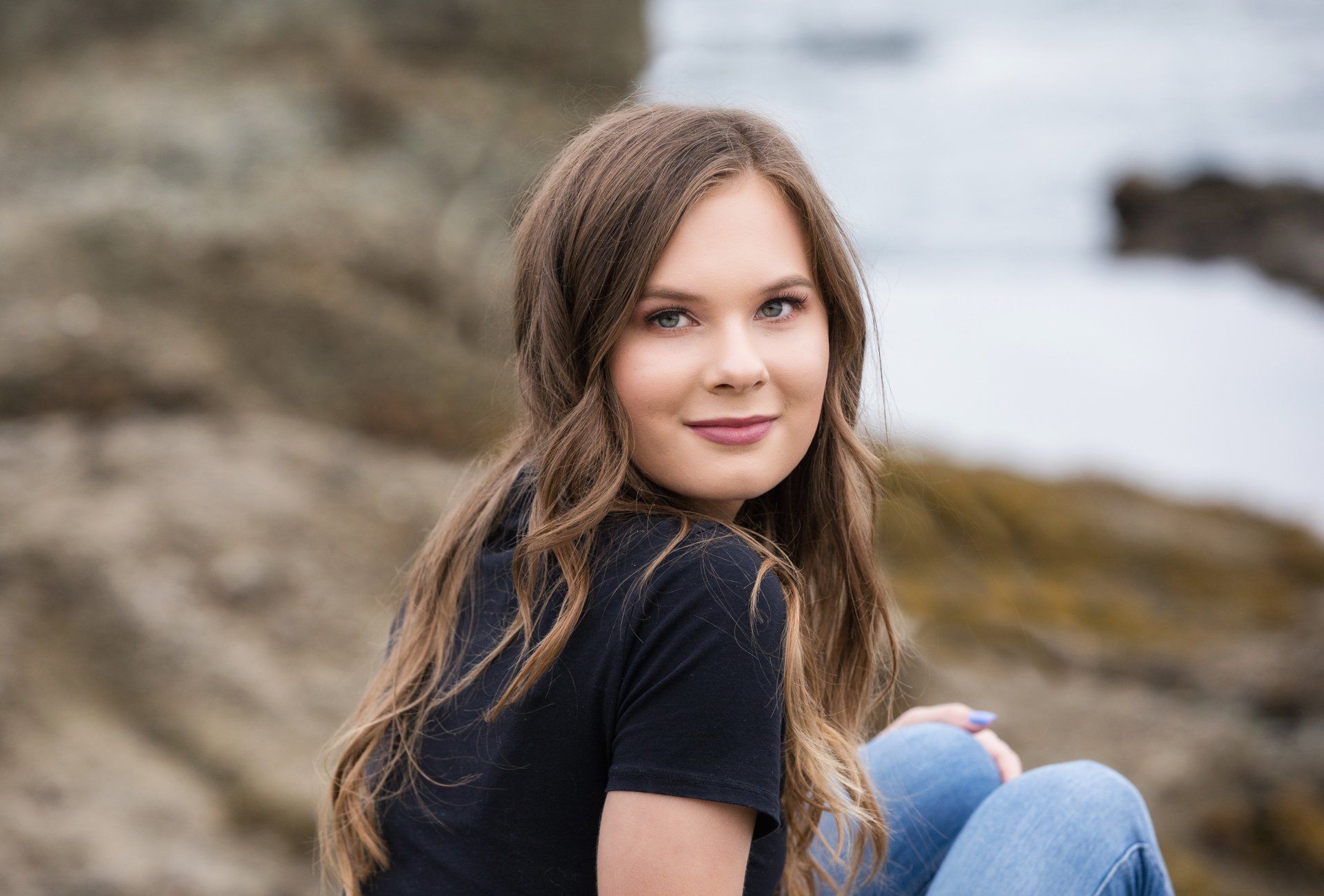 A young woman is sitting on a rock near the ocean.