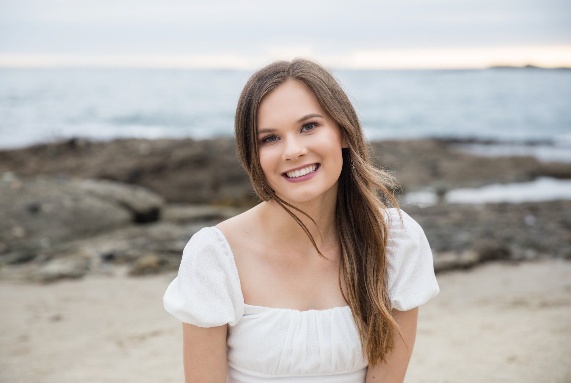 A woman in a white dress is smiling on the beach.