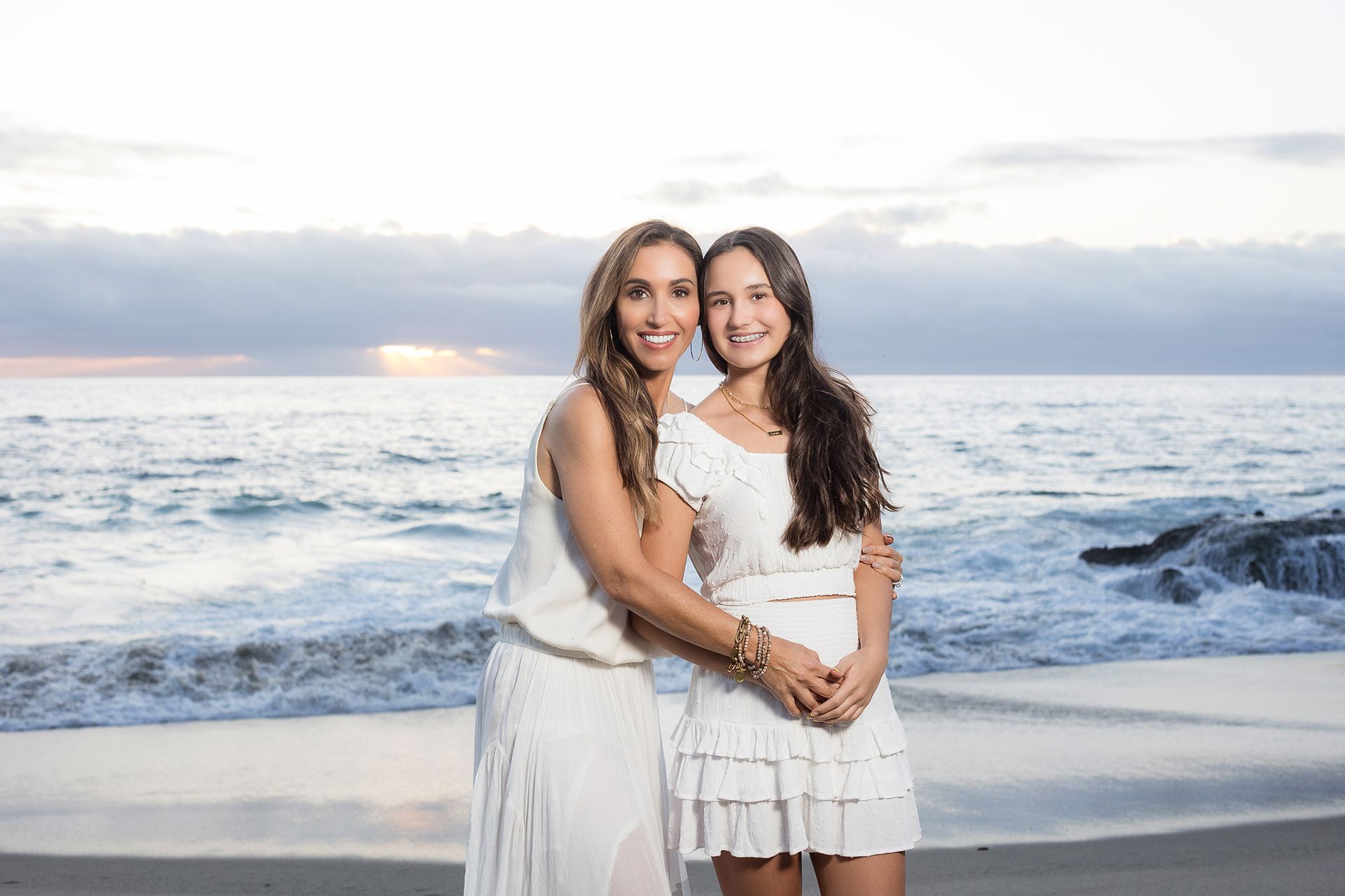 Mother and teenage daughter embracing by the ocean during a golden hour Laguna Beach session by an Orange County photographer.
