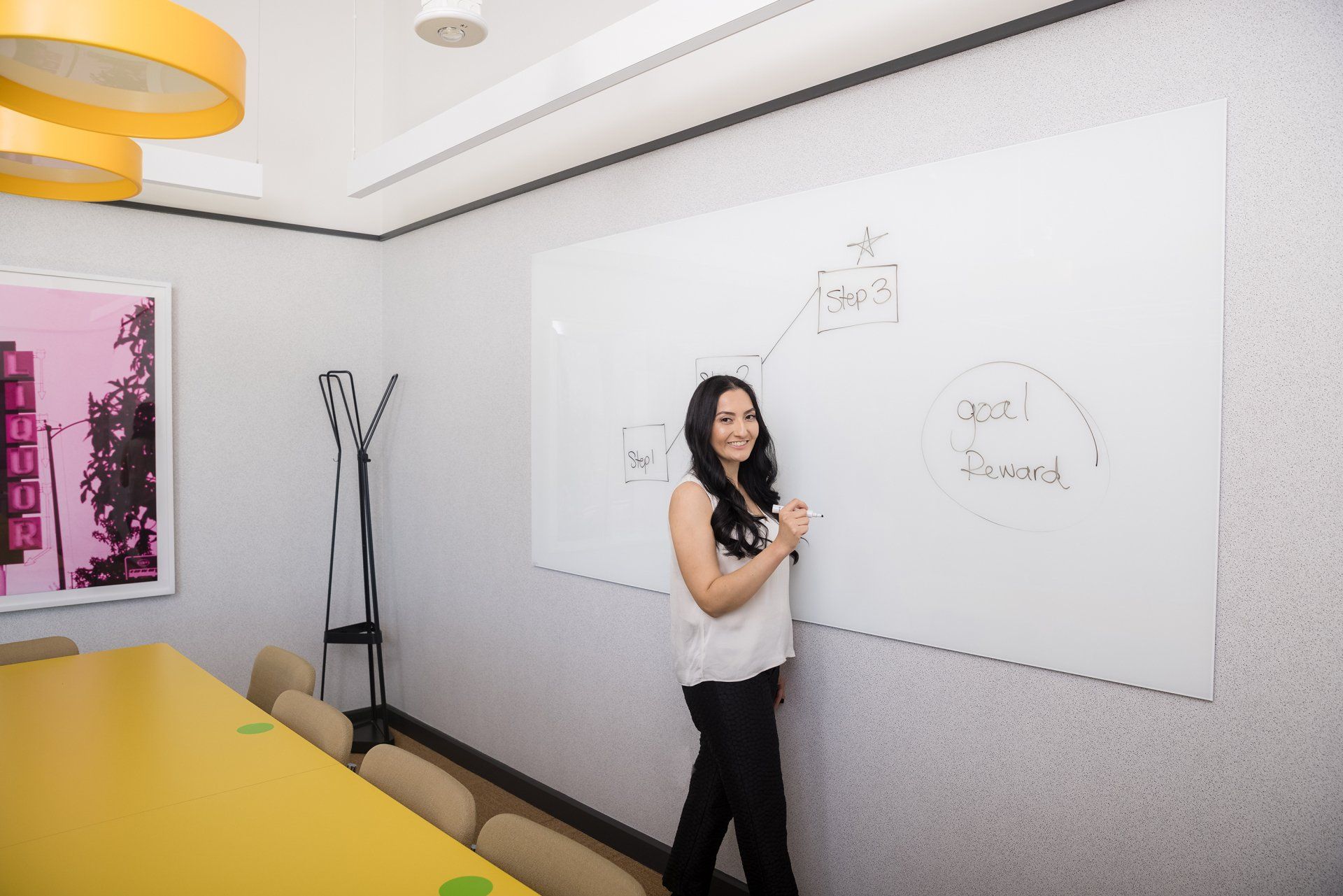A woman is standing in front of a whiteboard in a conference room.