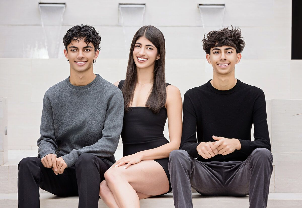 Three stylish siblings seated in front of a modern water feature, professionally captured for a luxury in-home portrait session in Newport Coast.