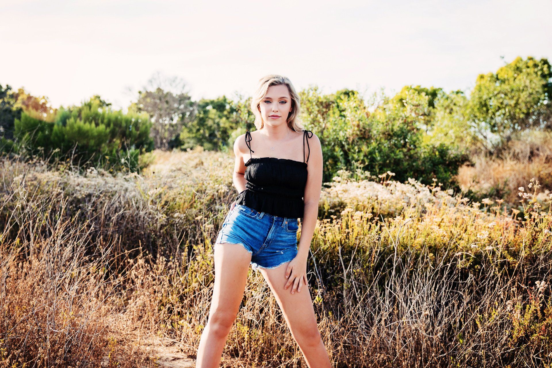 A woman in a black top and denim shorts is standing in a field.