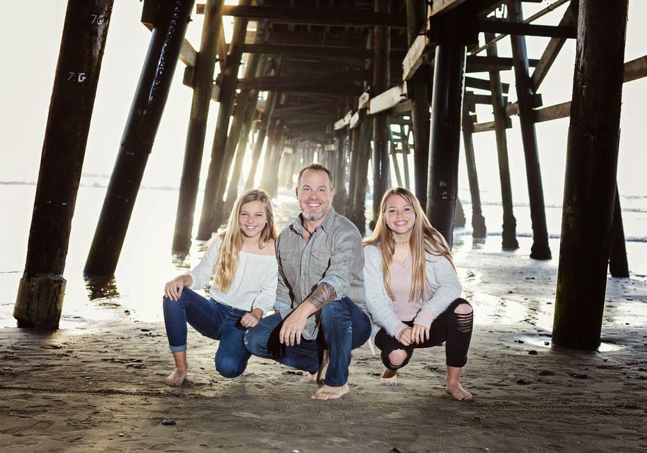 A man and two girls are posing for a picture under a pier.