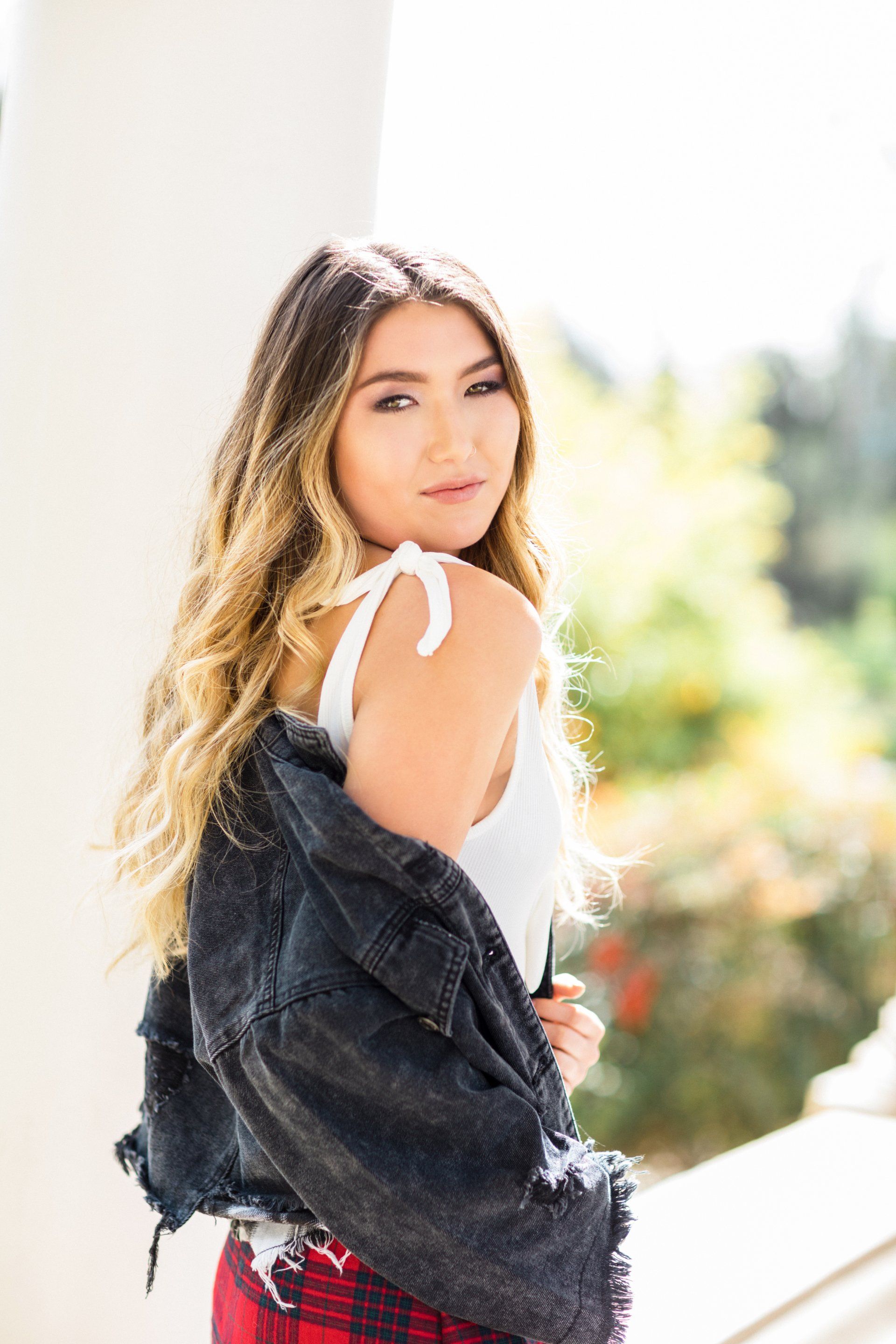 A woman wearing a black denim jacket and a white tank top is standing on a balcony.