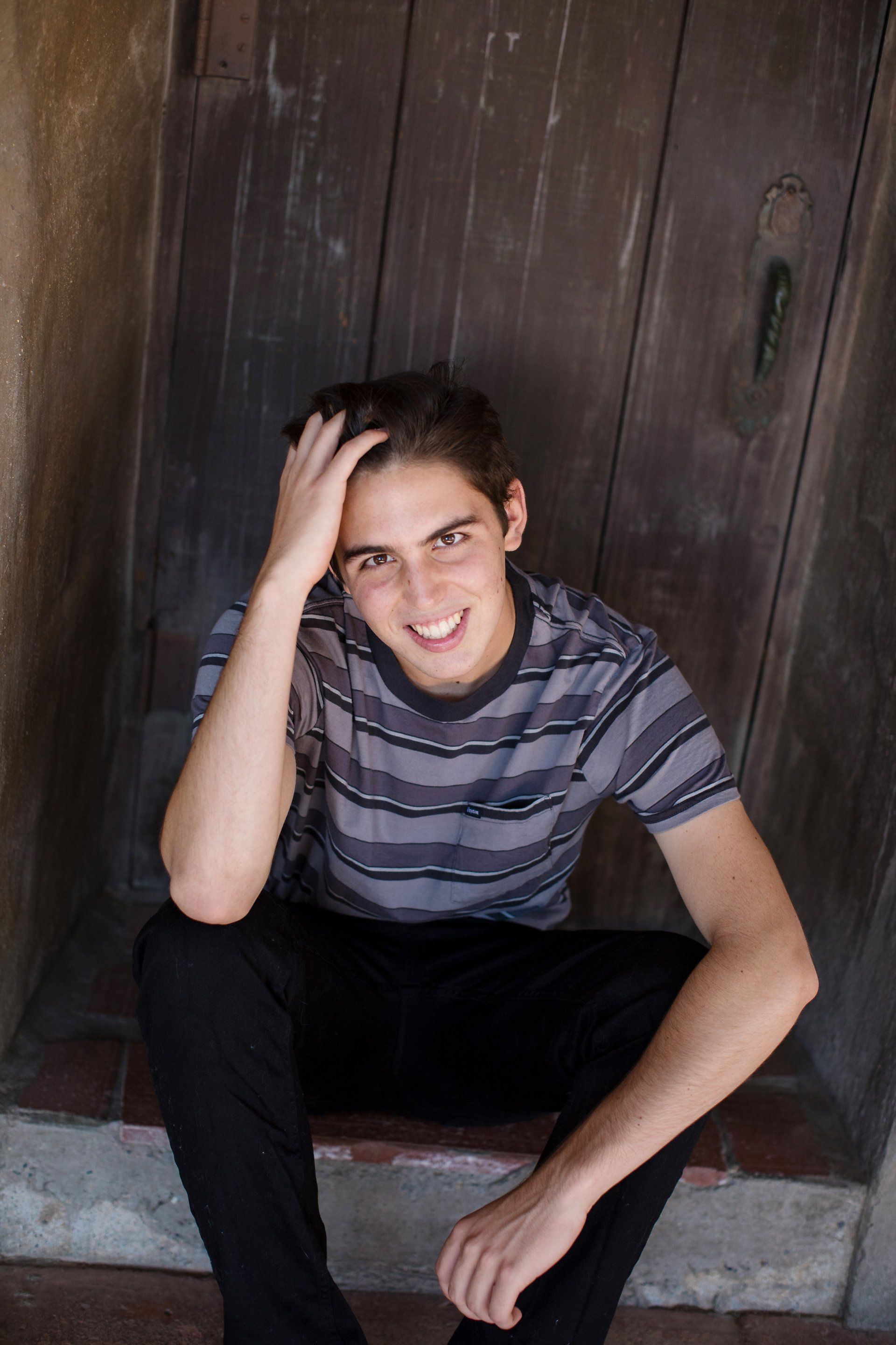 A young man is sitting on the steps of a building with his hand on his head.