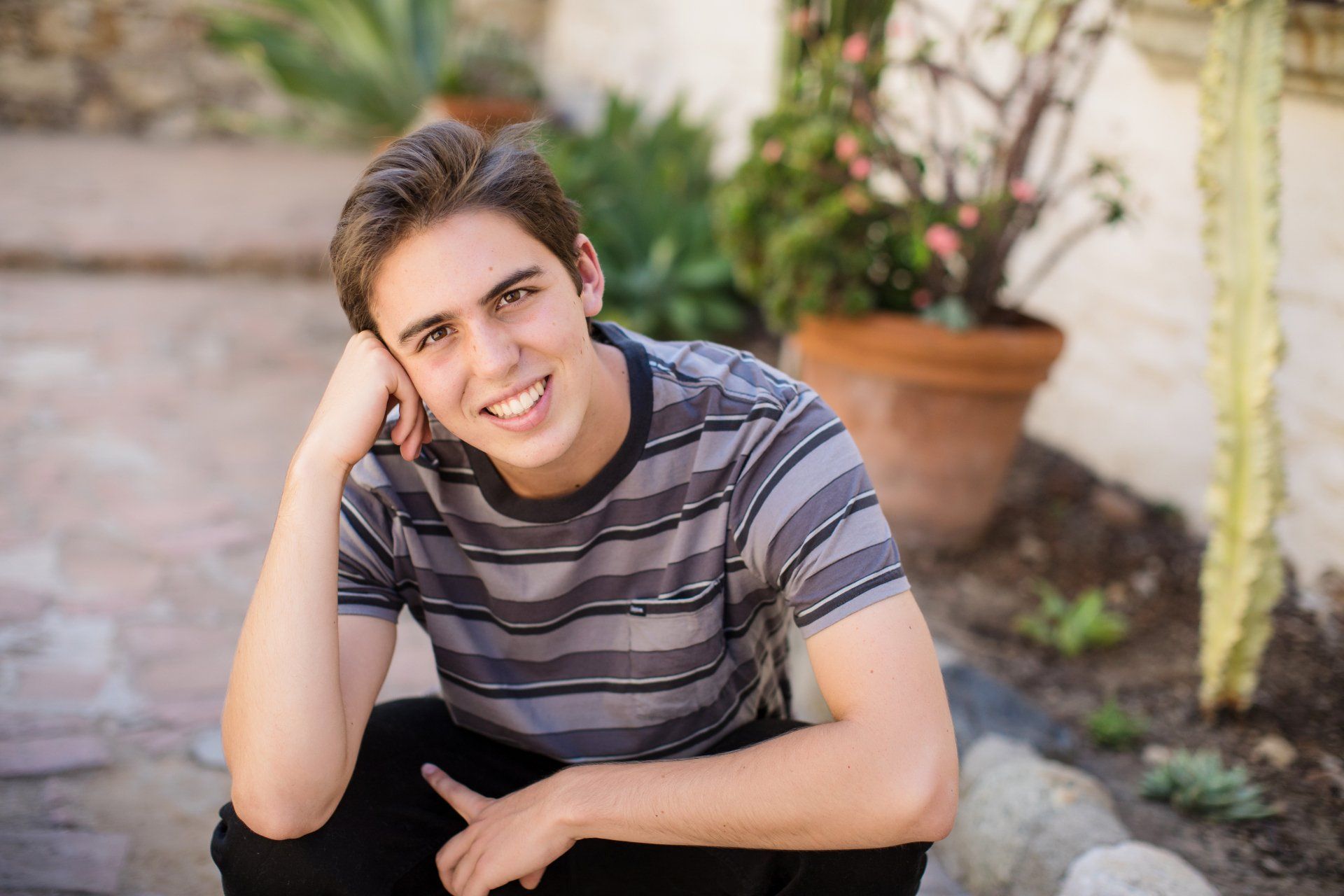 A young man is sitting on the ground with his hand on his chin and smiling.