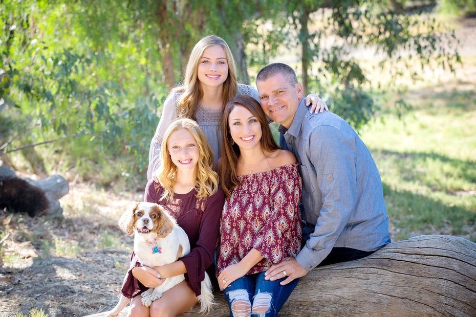 A family is posing for a picture with their dog while sitting on a hay bale.