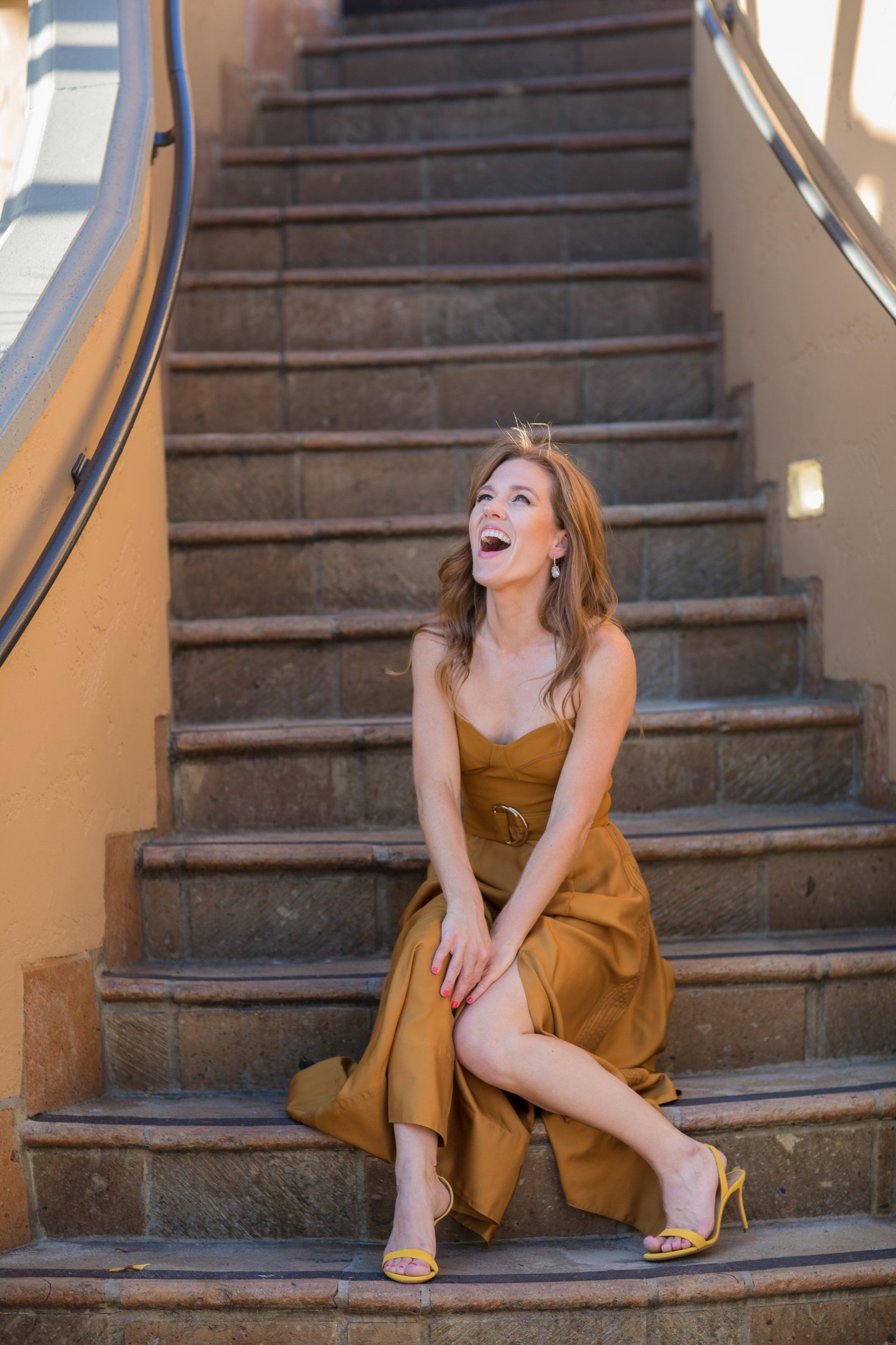 A woman in a gold dress is sitting on a set of stairs.