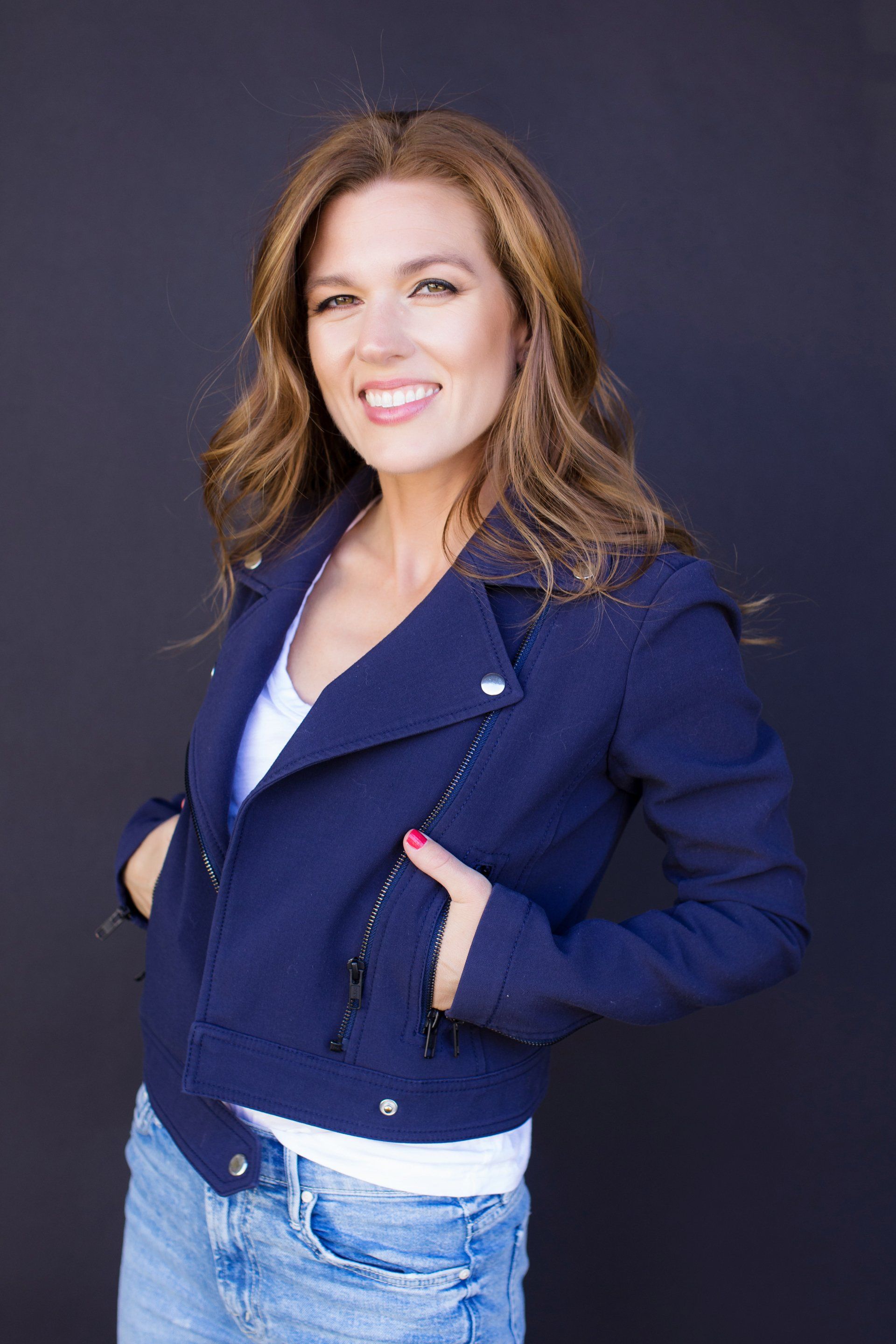 A woman is wearing a blue jacket and jeans and smiling.