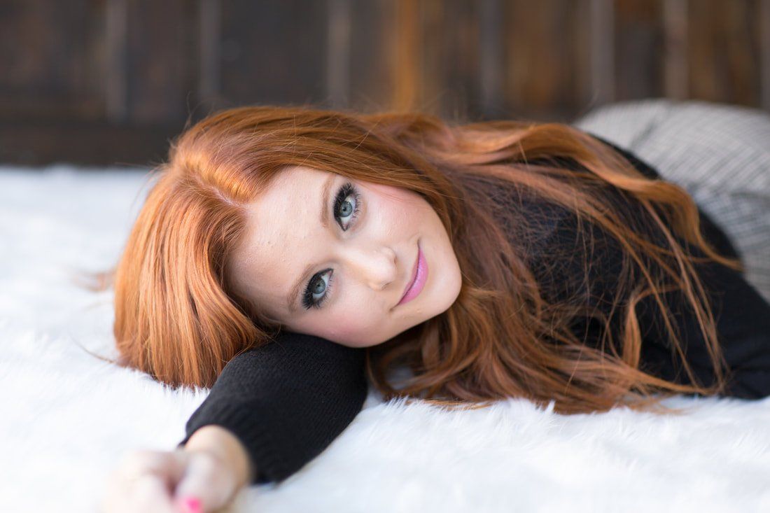 A woman with red hair is laying on a white blanket.