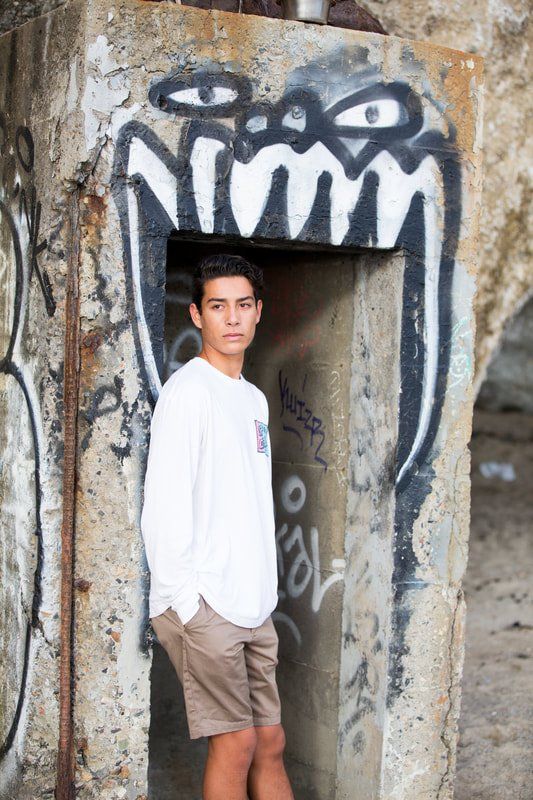 A young man is standing in front of a wall with graffiti on it.
