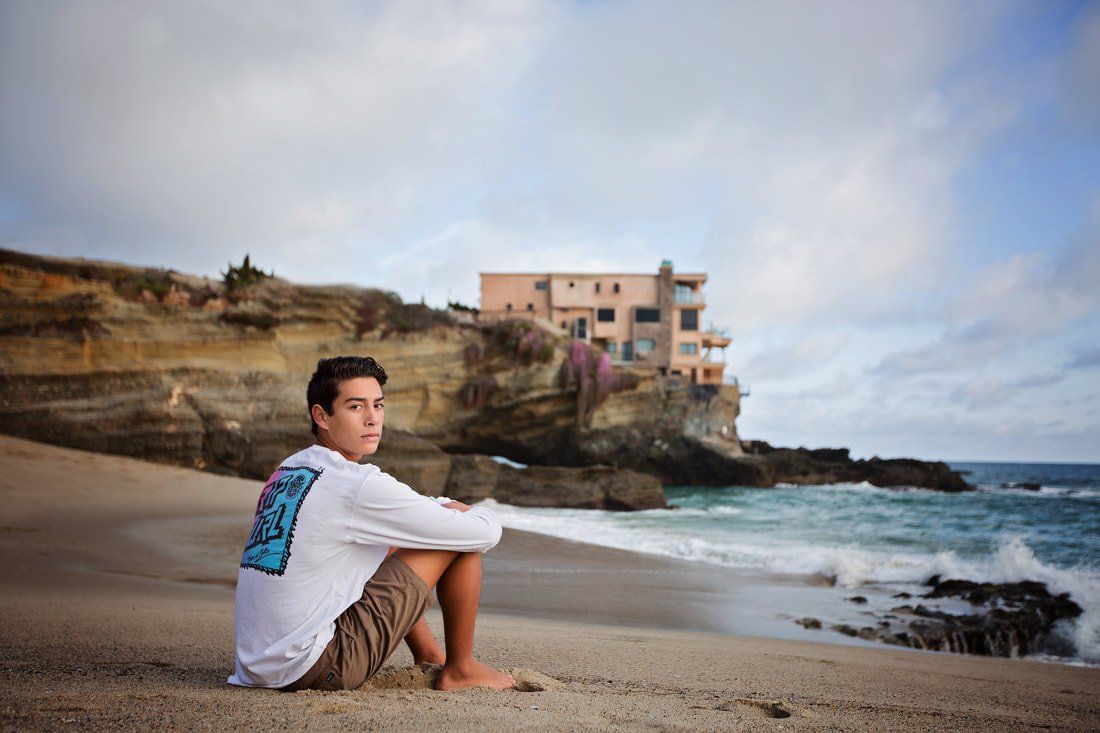 A man is sitting on the beach looking at the ocean.