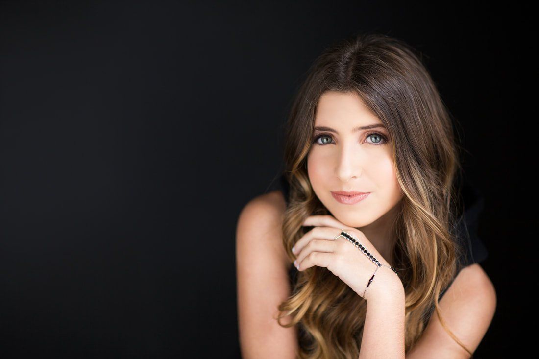 A woman is sitting with her hand on her chin and looking at the camera.