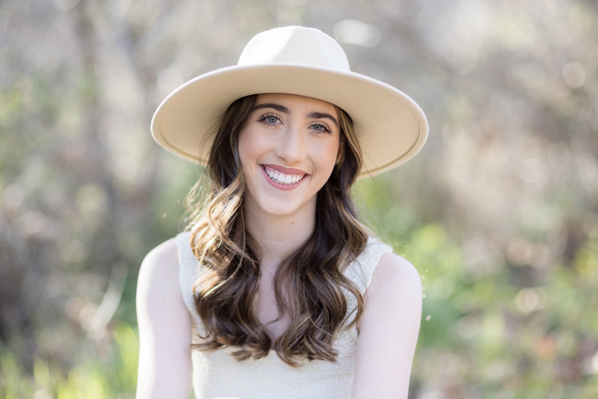 A woman wearing a hat and a white dress is smiling for the camera.
