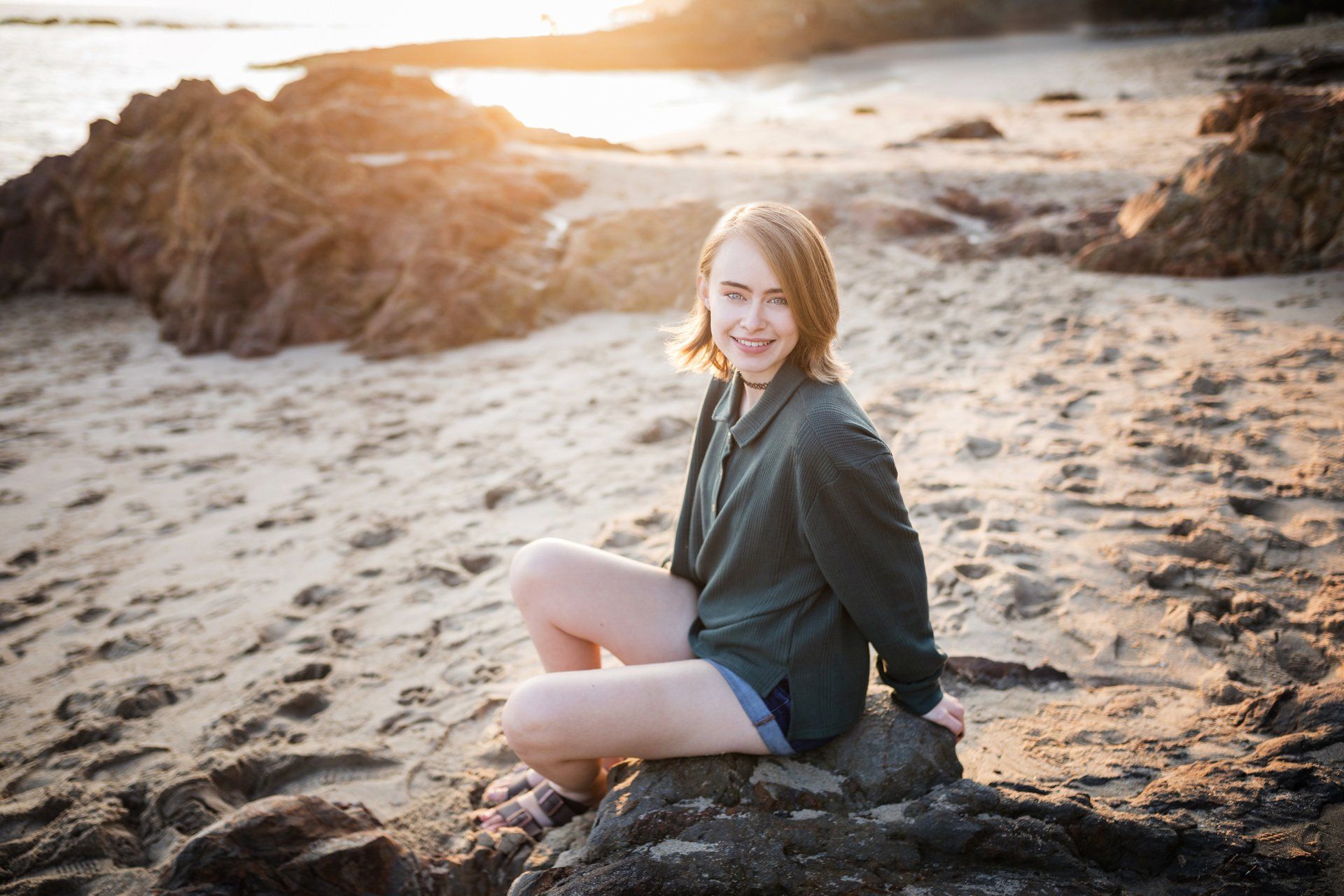 A young woman is sitting on a rock on the beach.