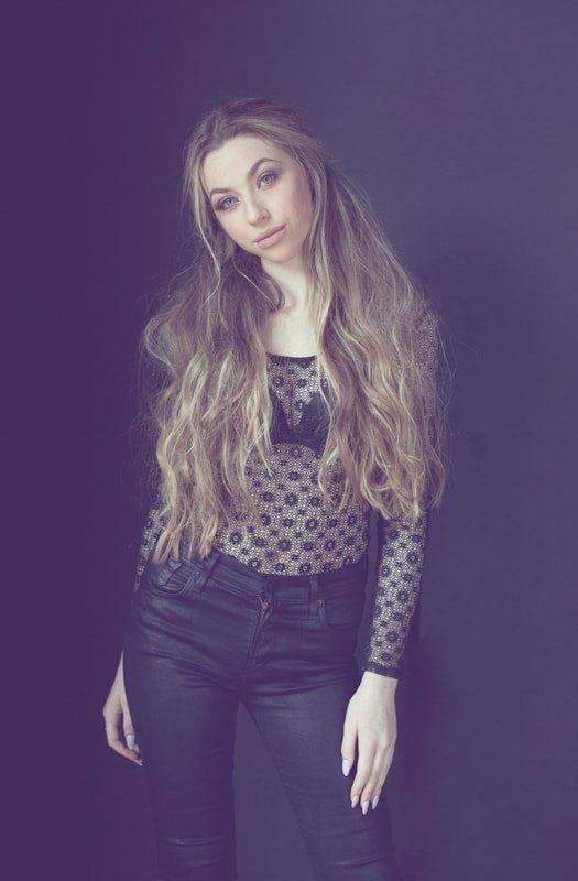 A woman with long hair is standing in front of a purple background.