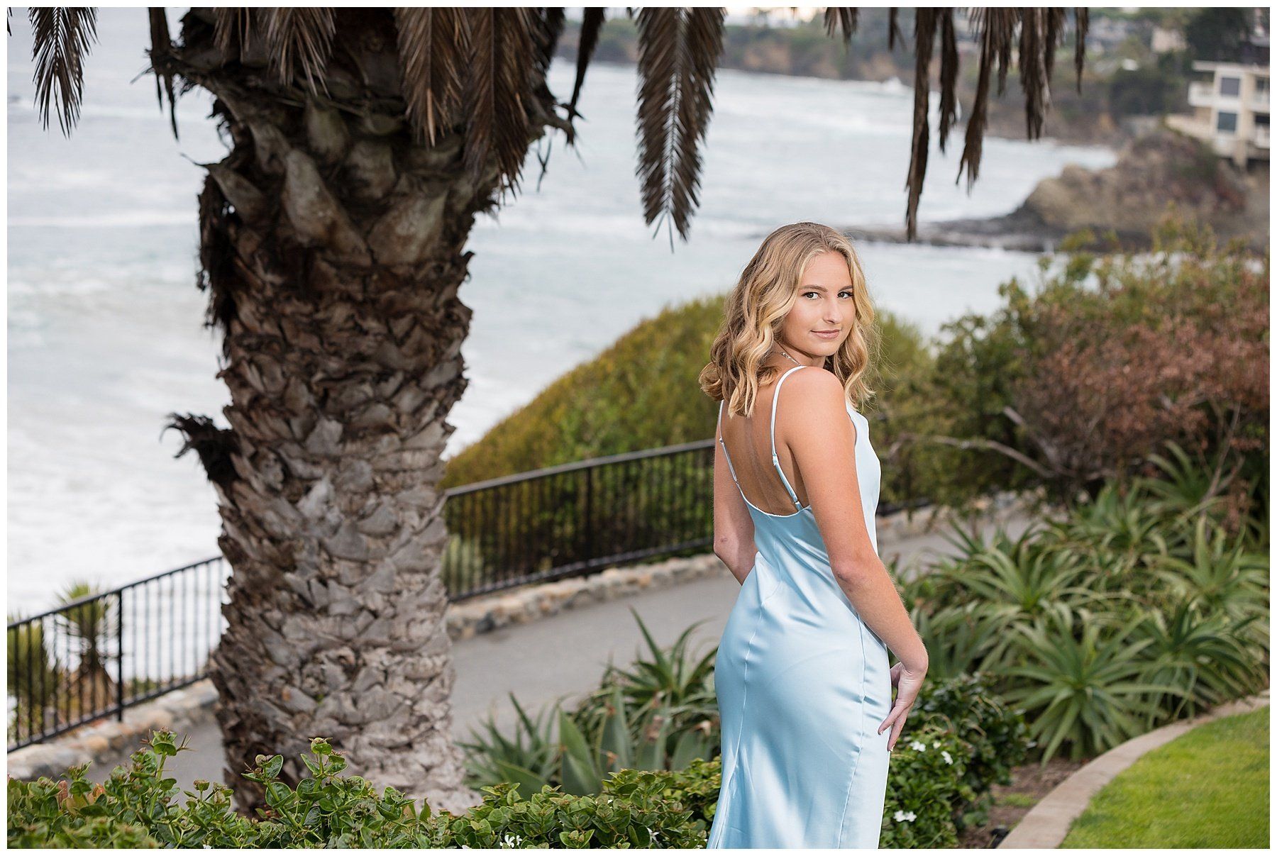 A woman in a blue dress is standing in front of a palm tree.