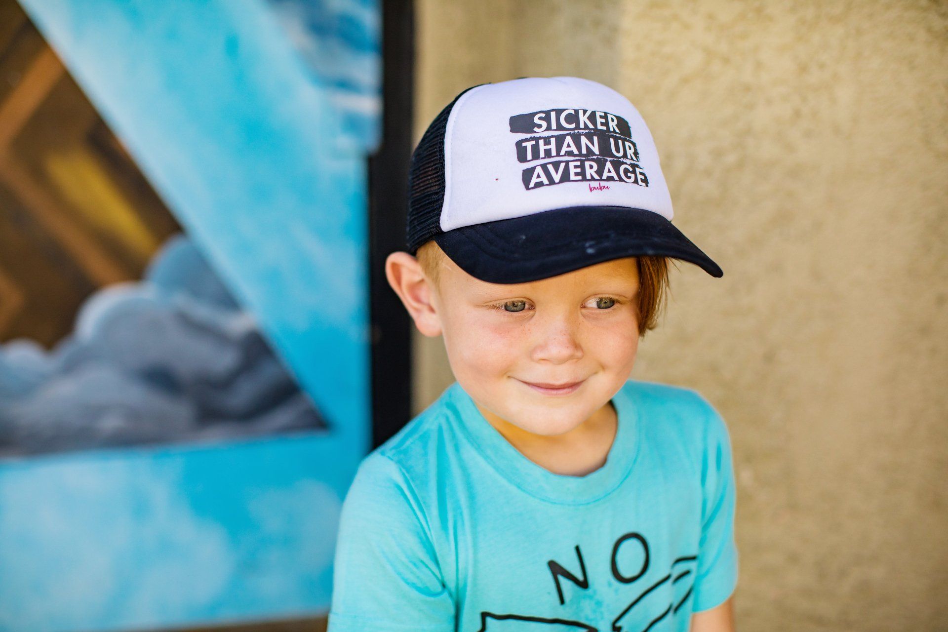 A young boy wearing a trucker hat and a blue shirt.
