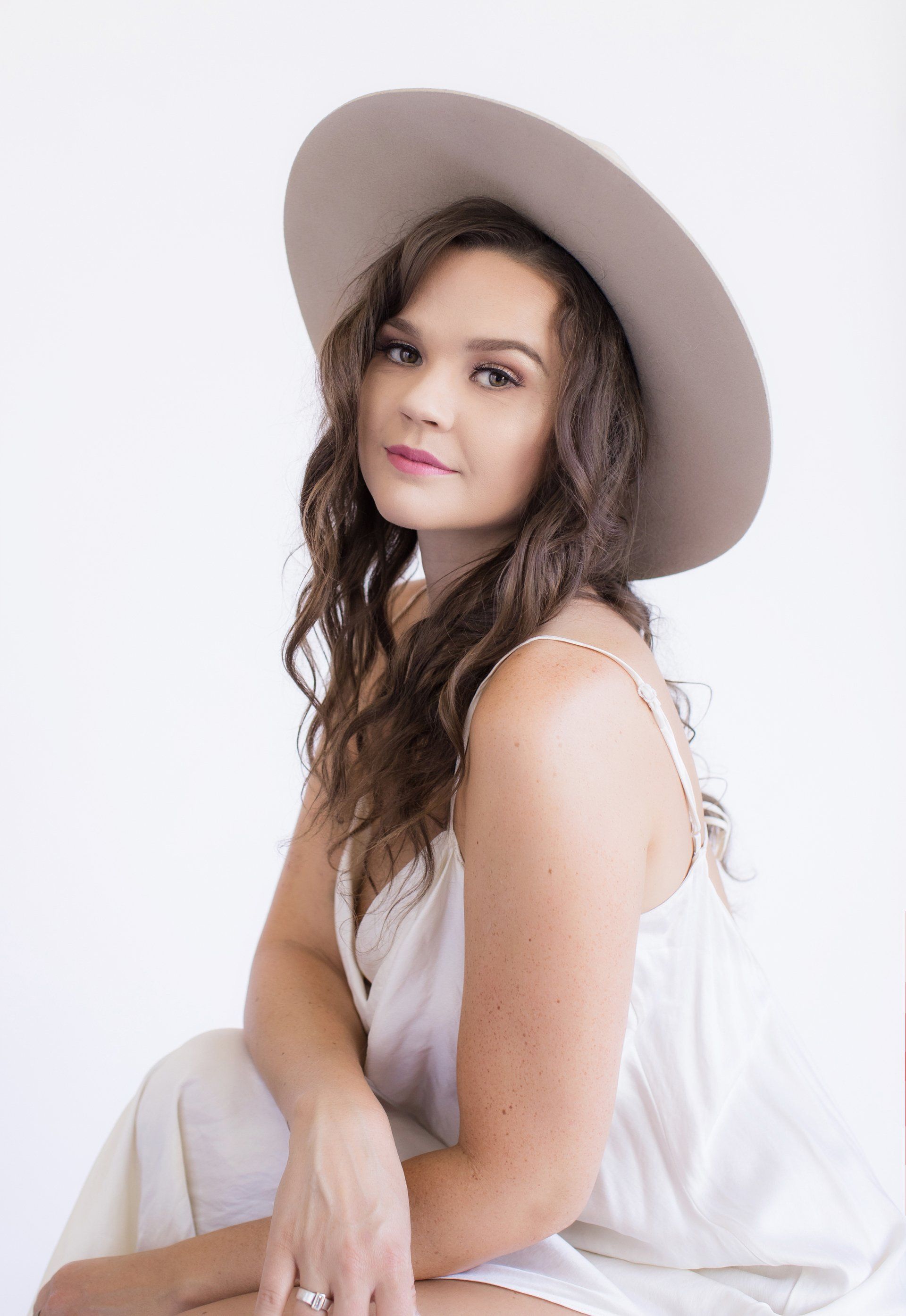 A woman wearing a hat and a white dress is sitting down.