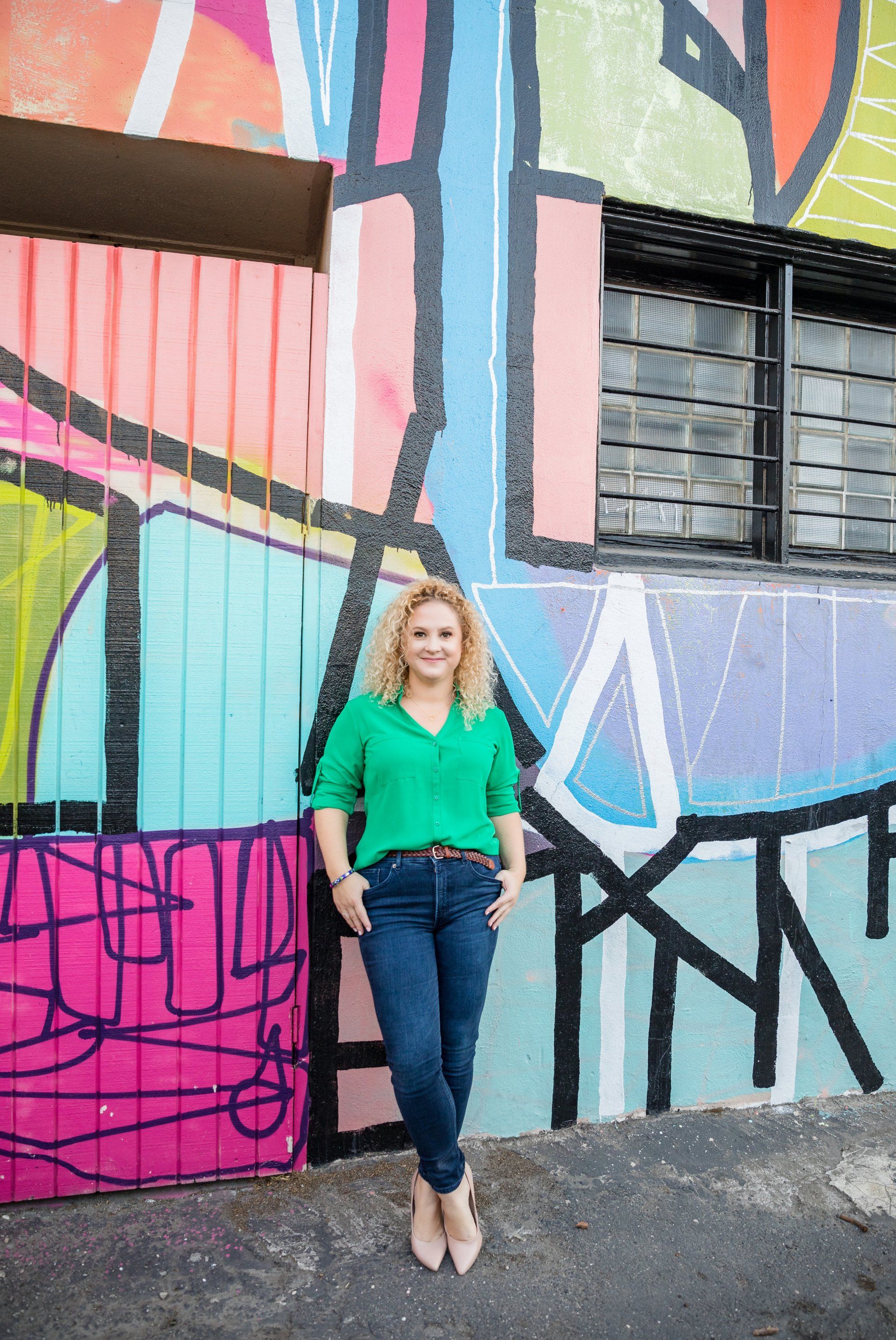 A woman is standing in front of a colorful graffiti wall.