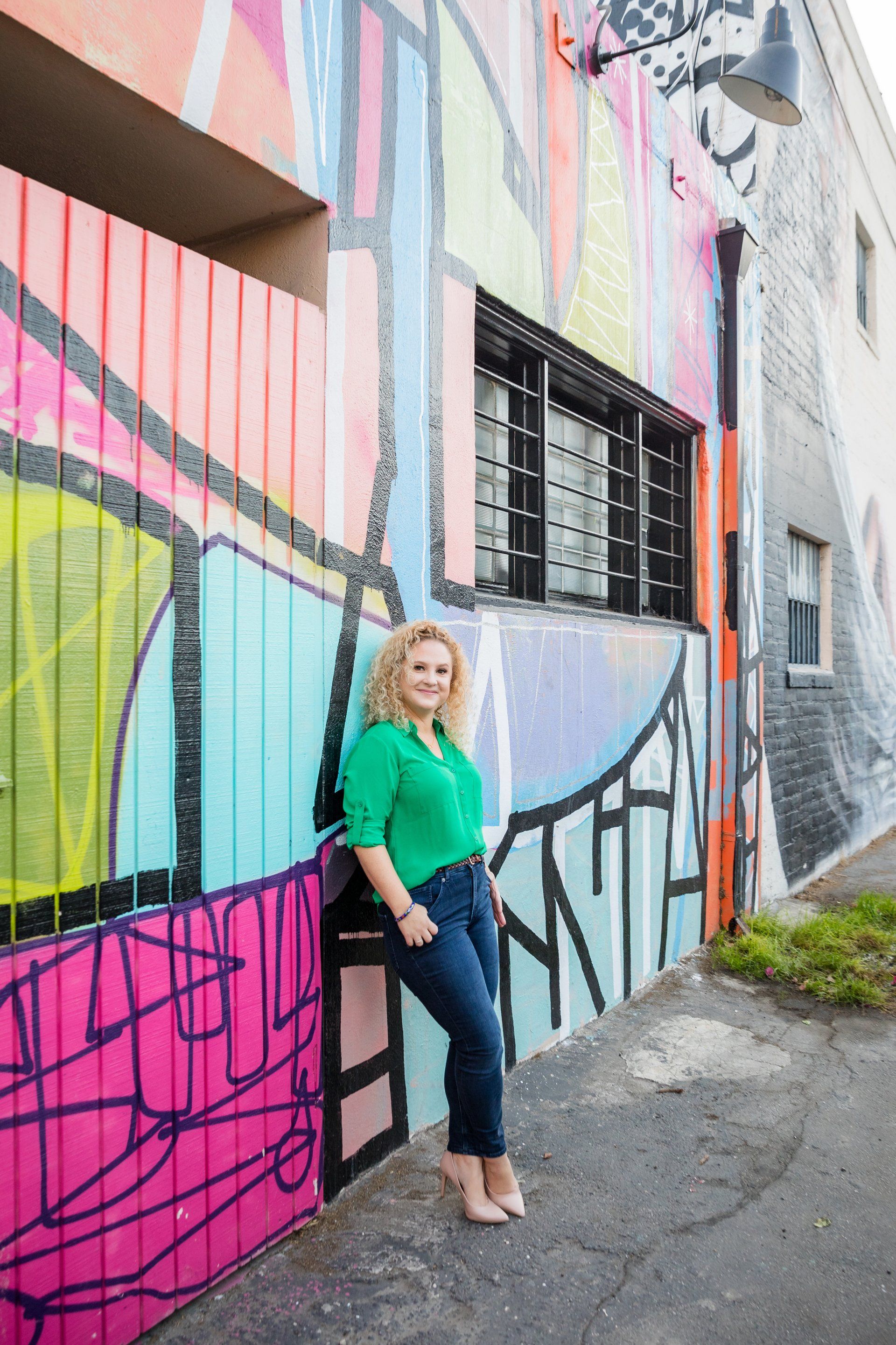 A woman is leaning against a wall with graffiti on it.