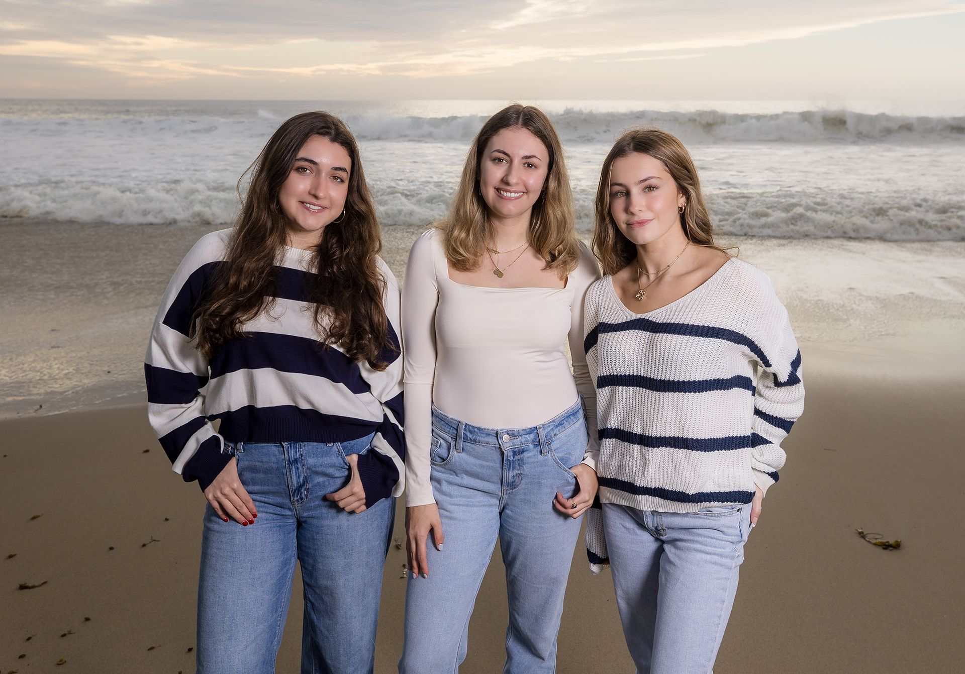 Three sisters in navy, cream and white outfits posing in front of the ocean at Salt Creek at sunset.