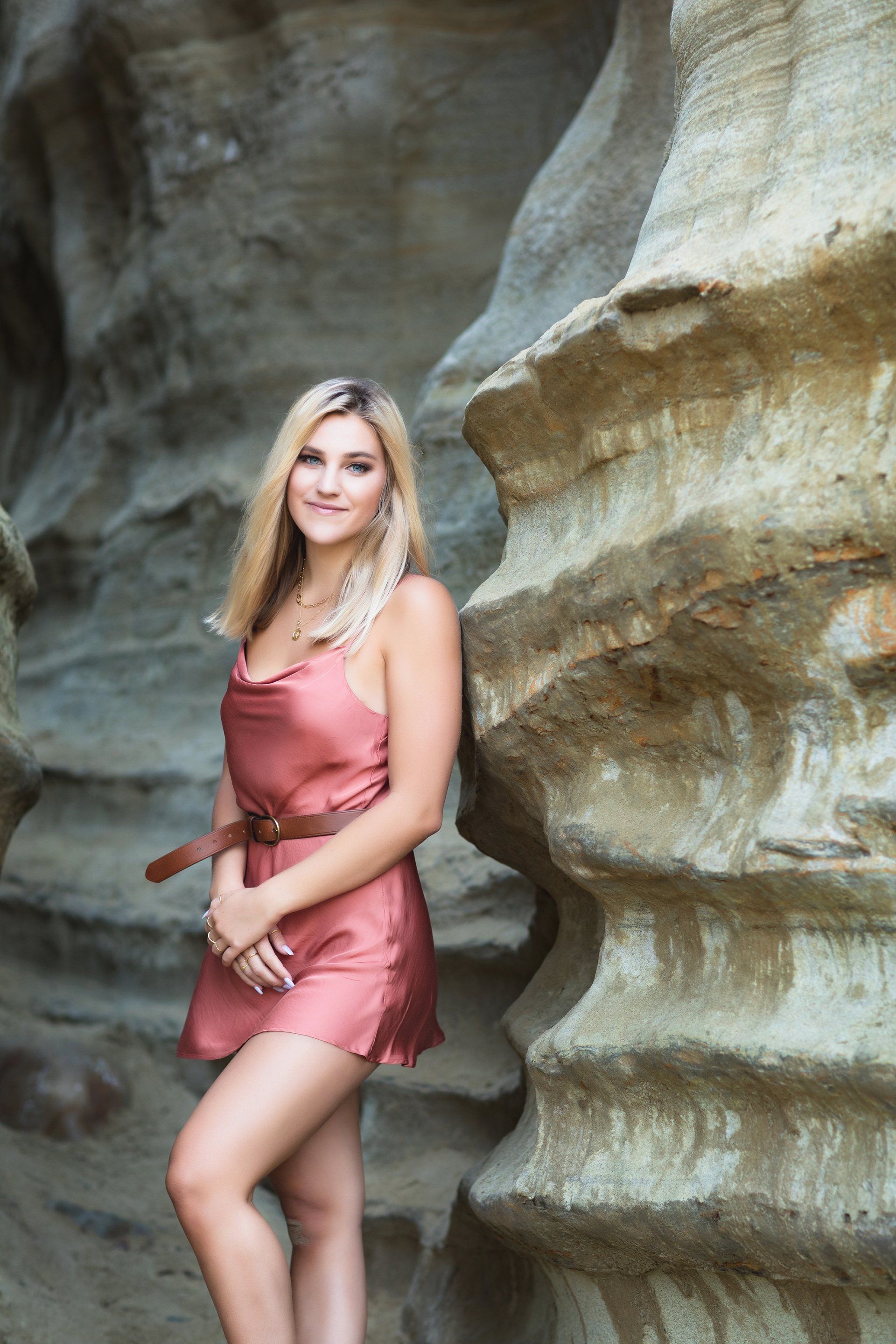 A woman in a pink dress is standing next to a rock wall.