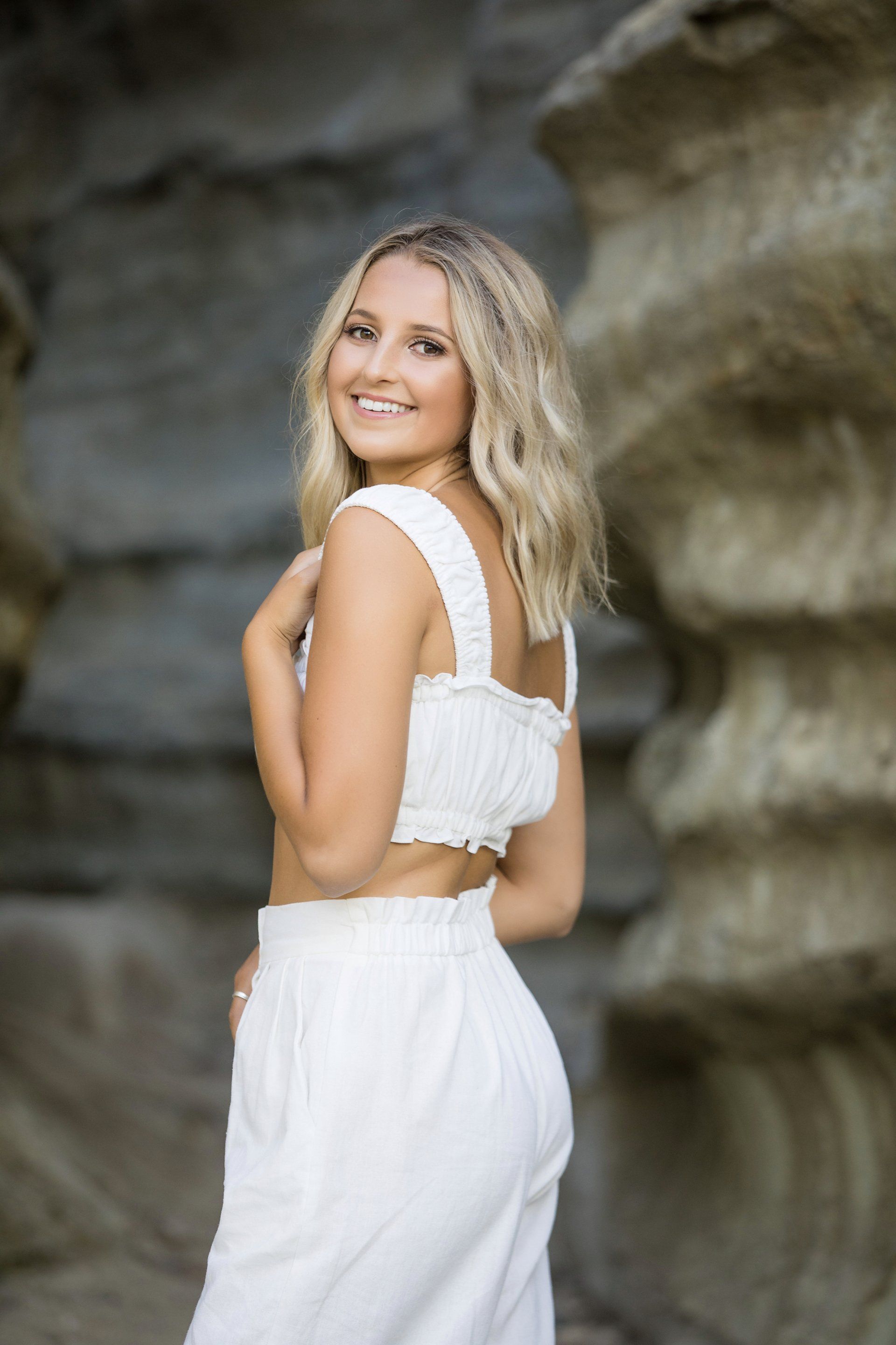 A woman in a white dress is standing in front of a rock formation.