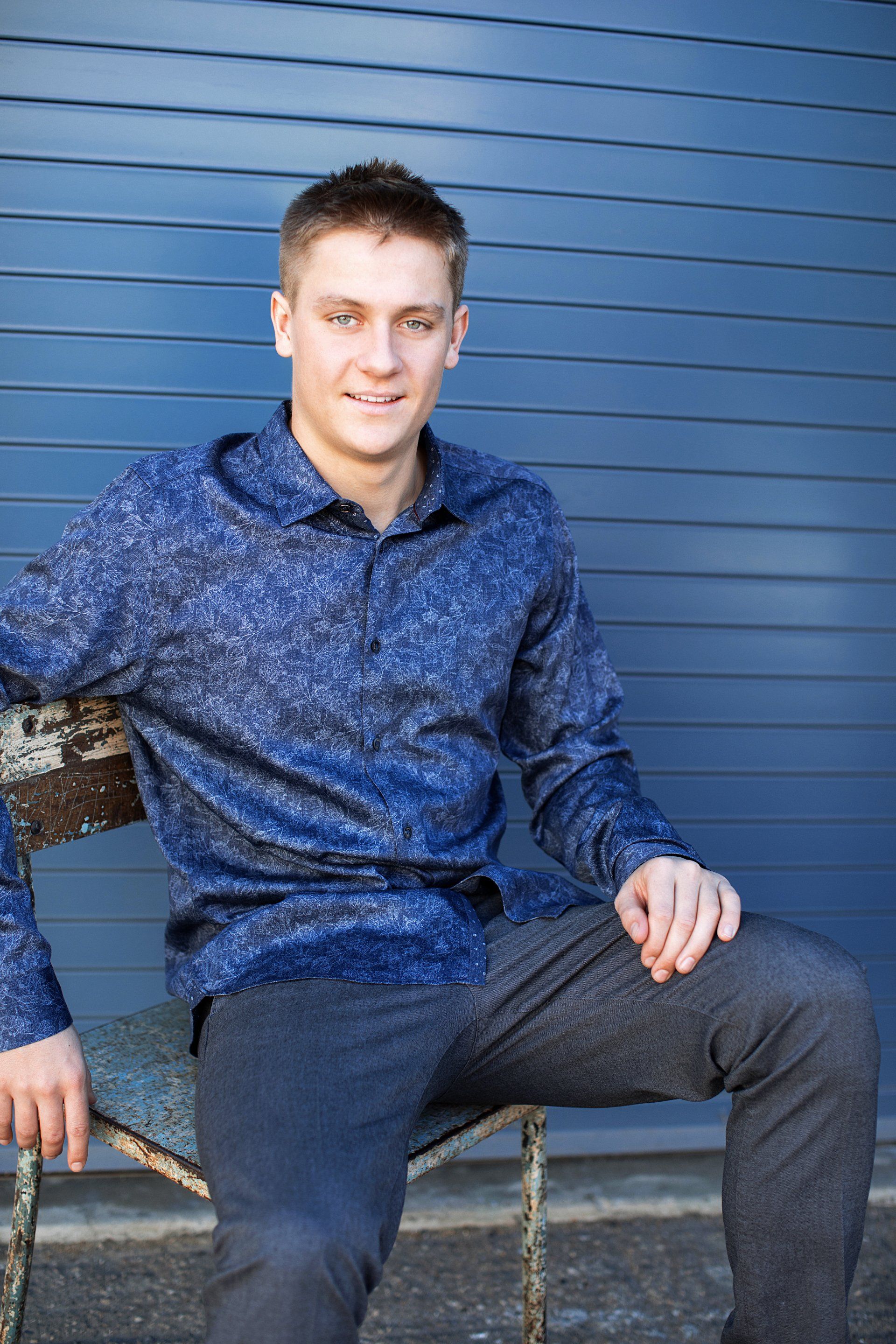 A young man is sitting on a bench in front of a blue wall.