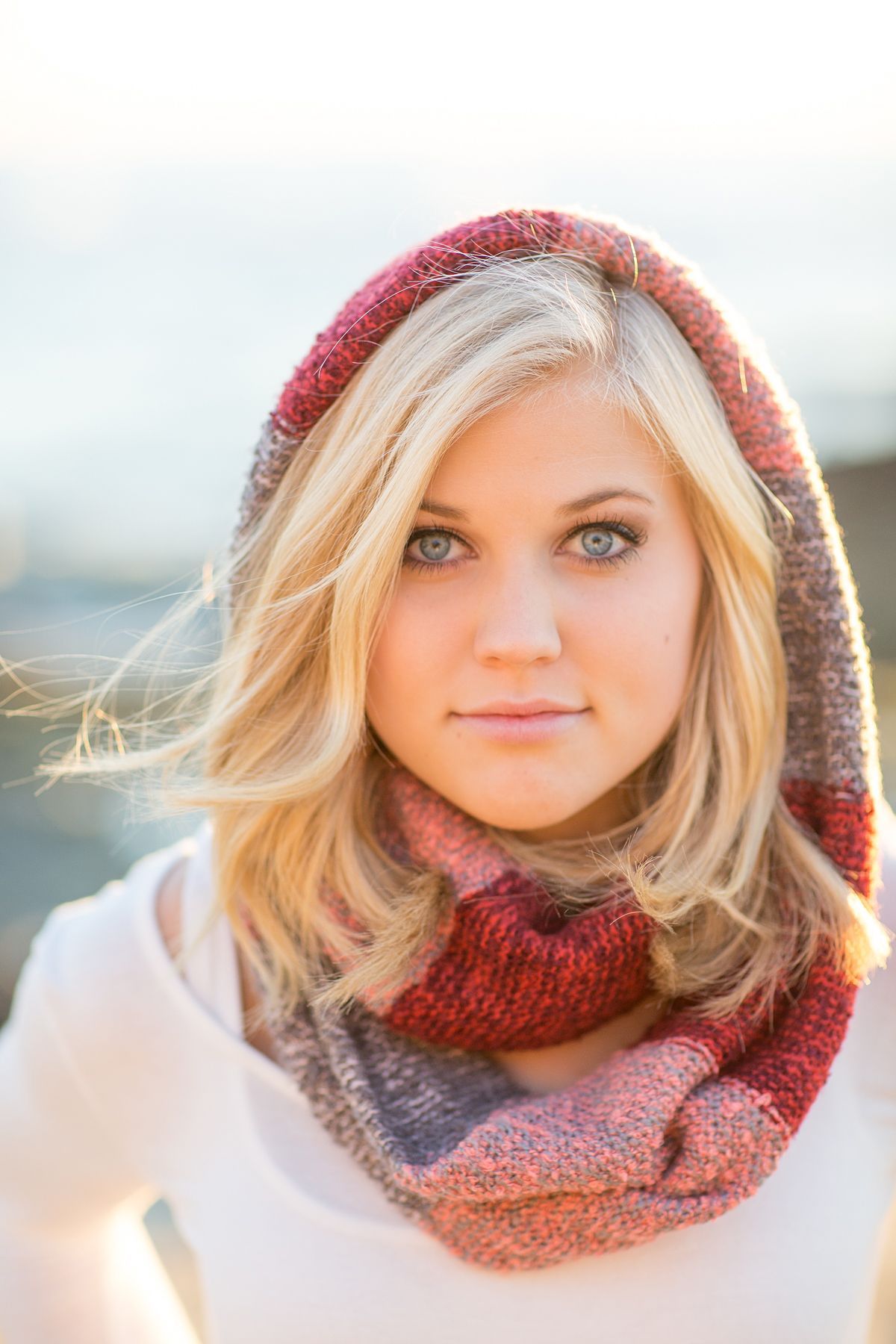 Girl posing at Victoria Beach in front of the ocean wearing a scarf around her neck and head.