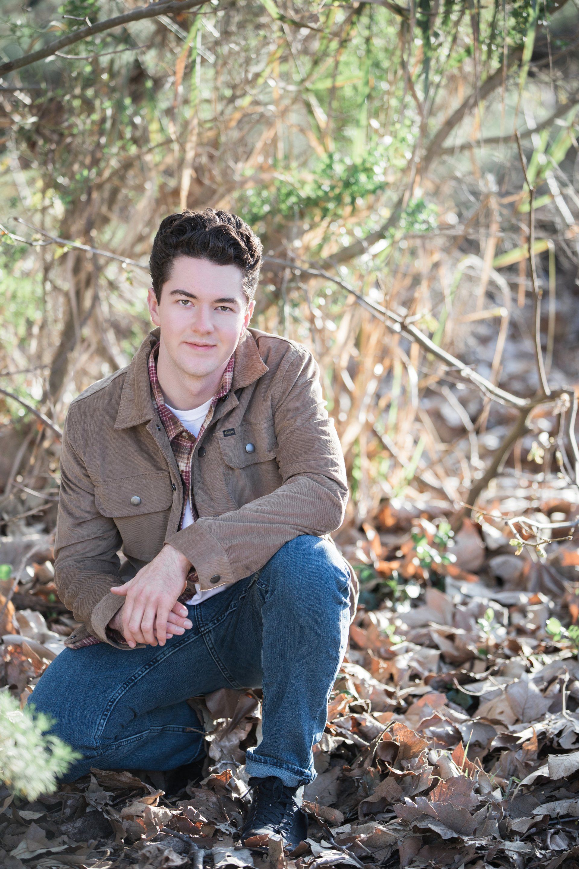 A young man is kneeling down in the woods.