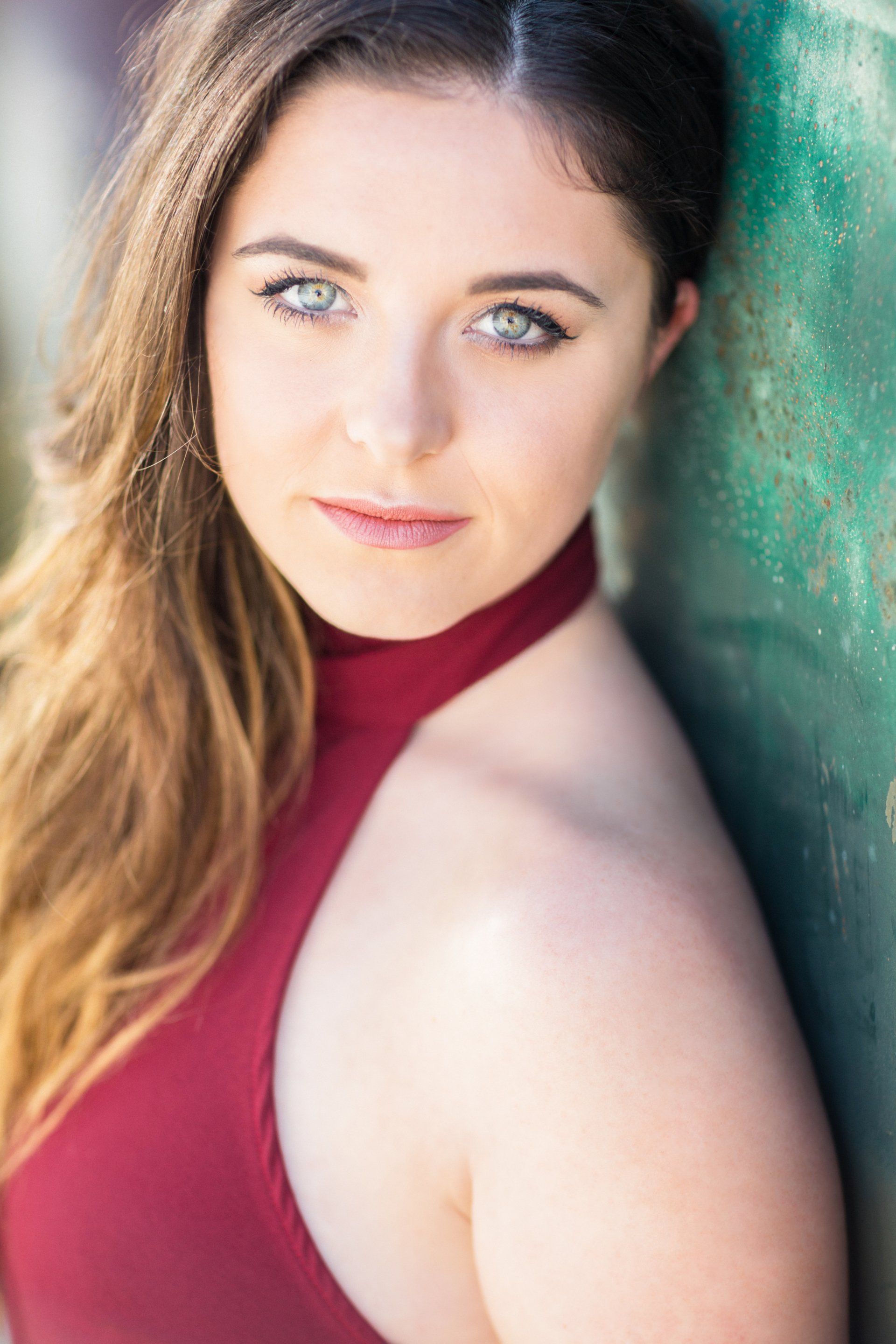 A woman in a red halter top is leaning against a green wall.