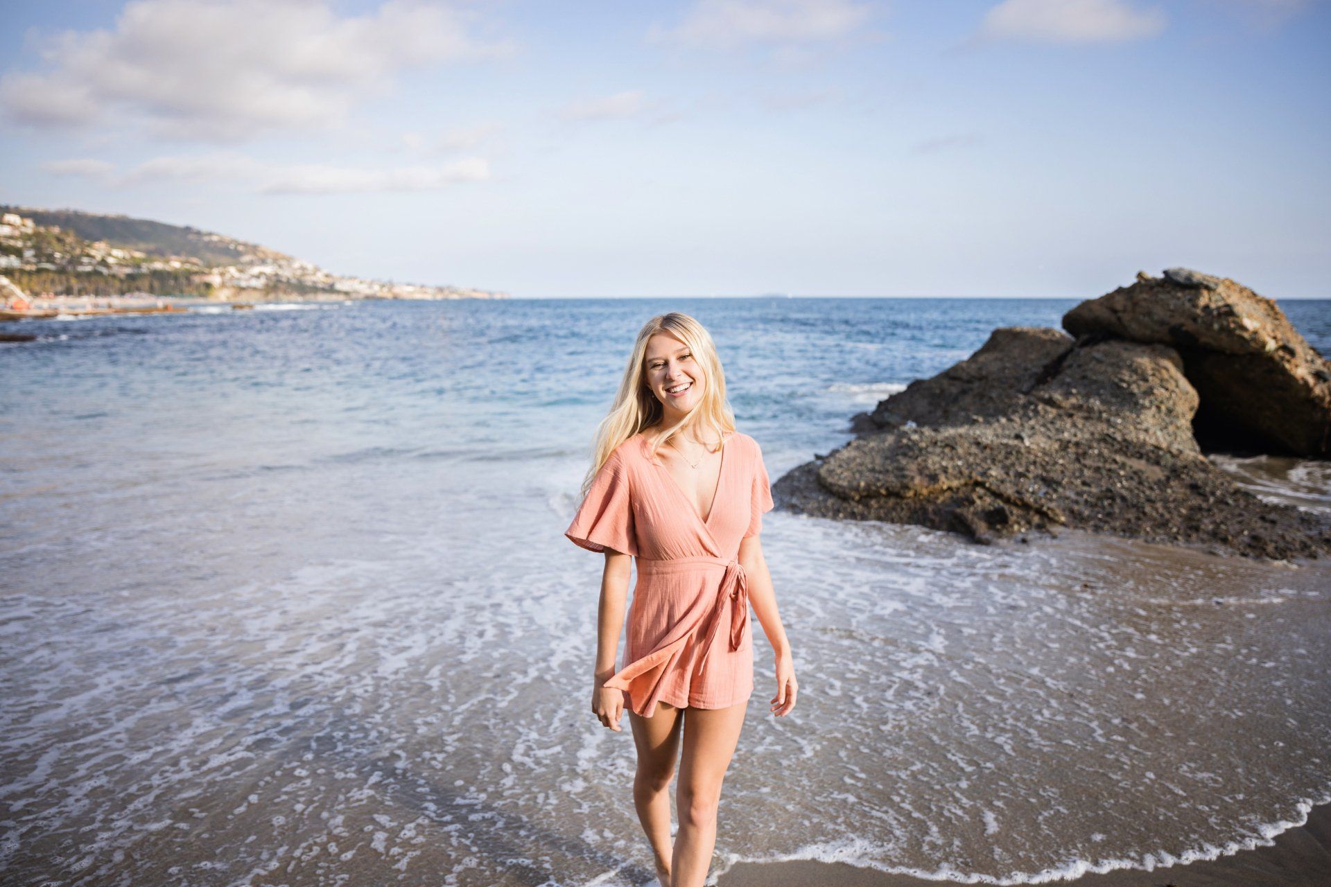 A woman in a pink dress is standing on a beach near the ocean.