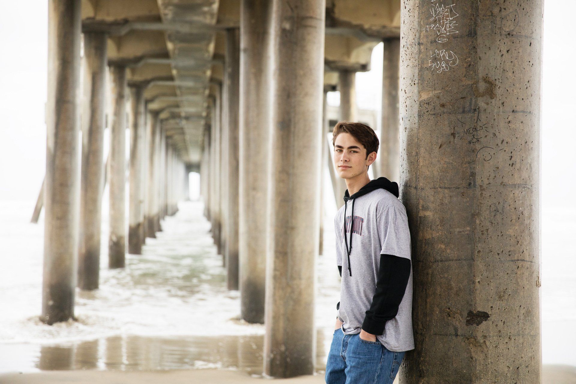 A young man is leaning against a pillar under a pier.