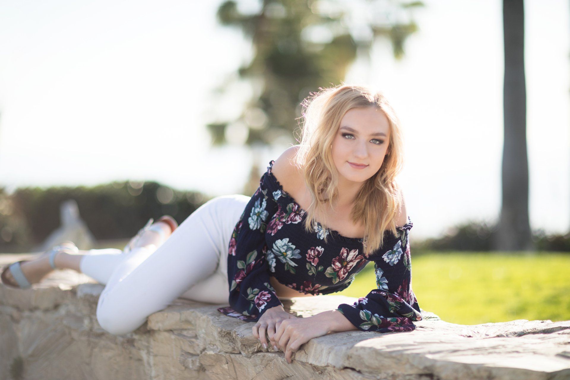 A young woman is laying on a rock in a park.