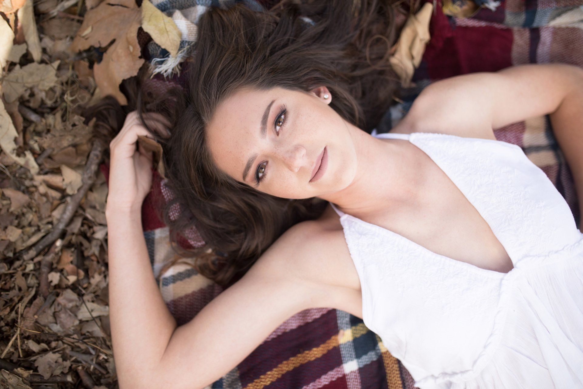 A woman in a white dress is laying on a plaid blanket.