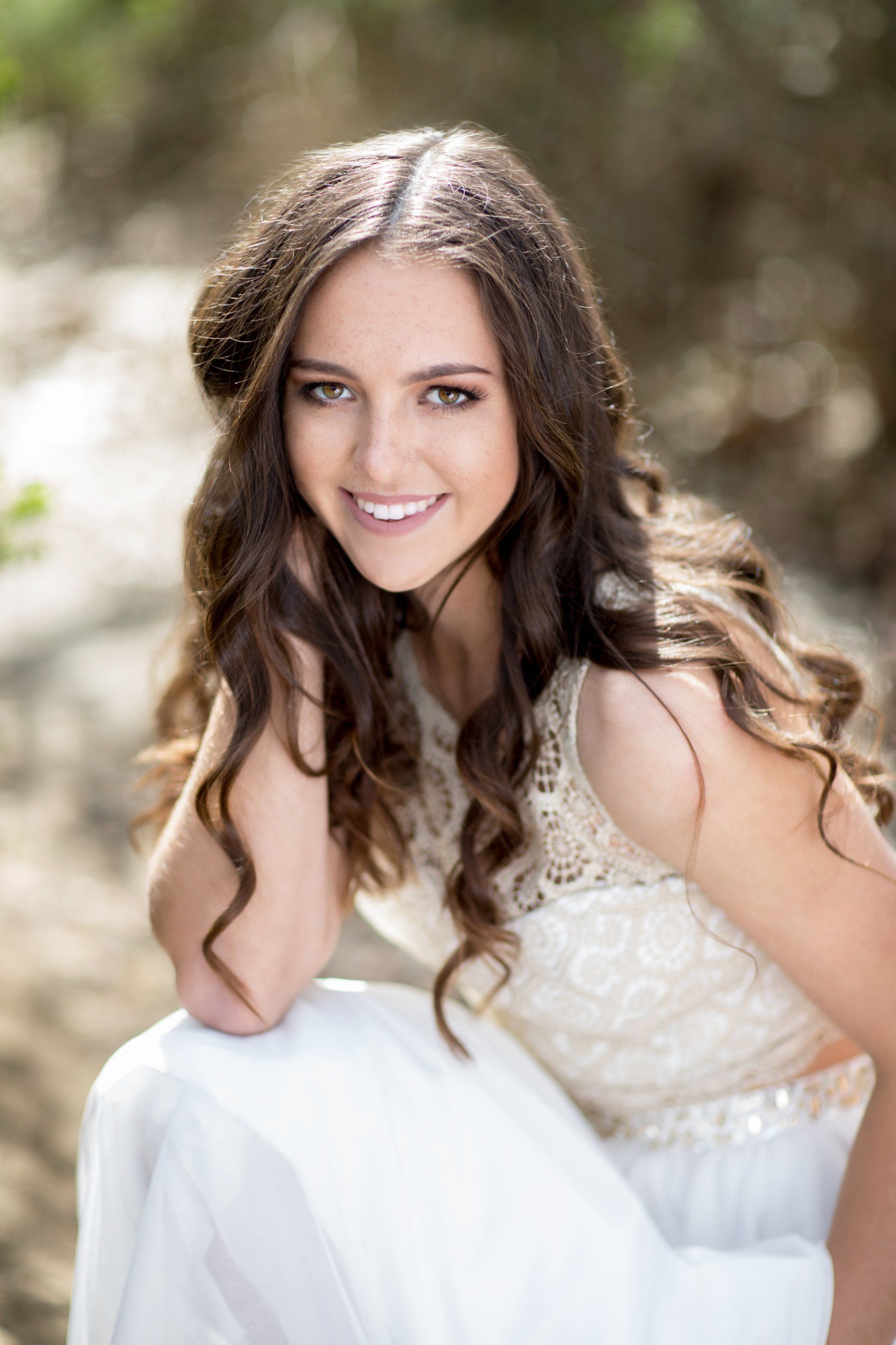 A woman in a white dress is sitting on the ground and smiling.