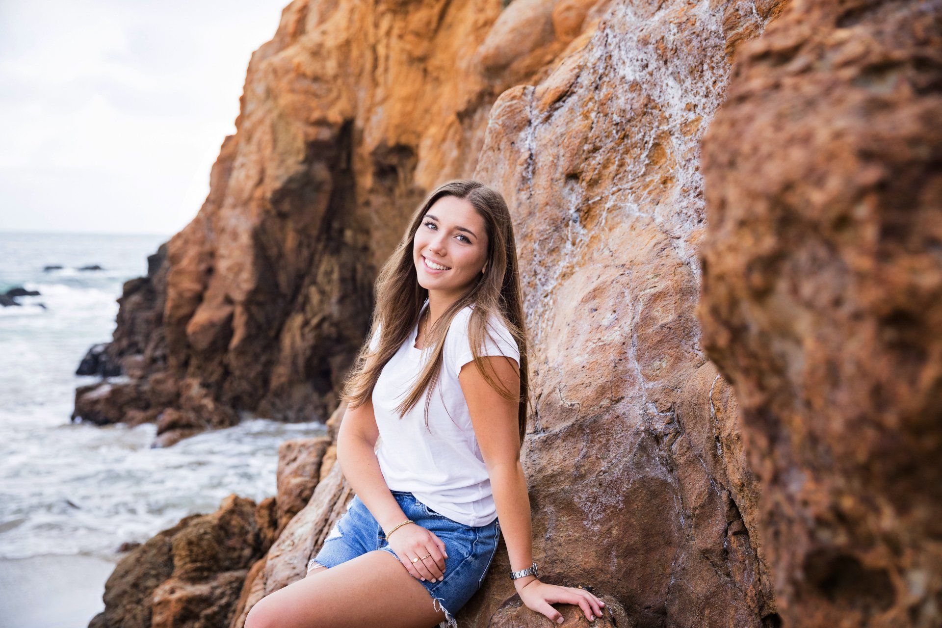 A young woman is sitting on a rock near the ocean.