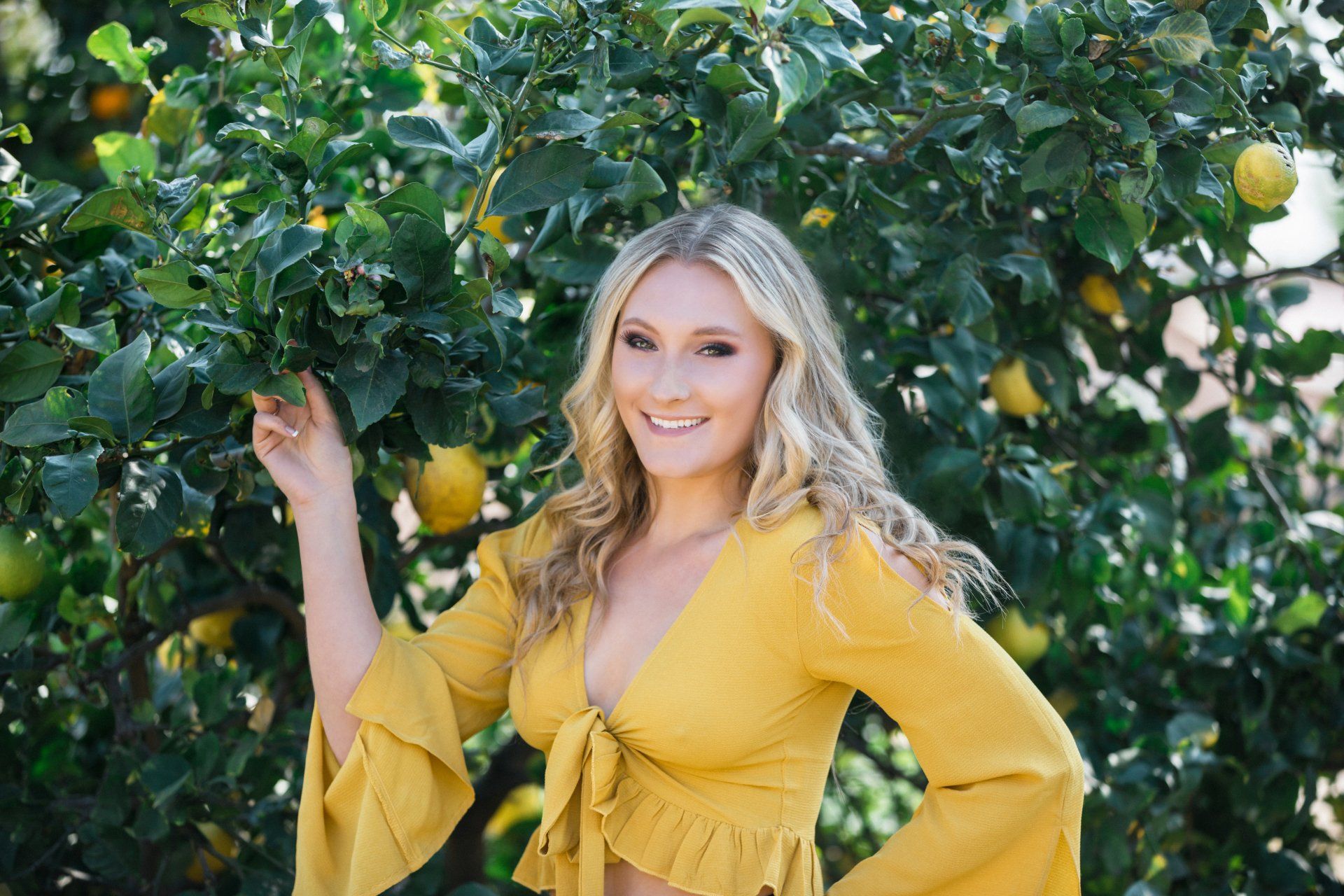 A woman in a yellow top is standing in front of a lemon tree.