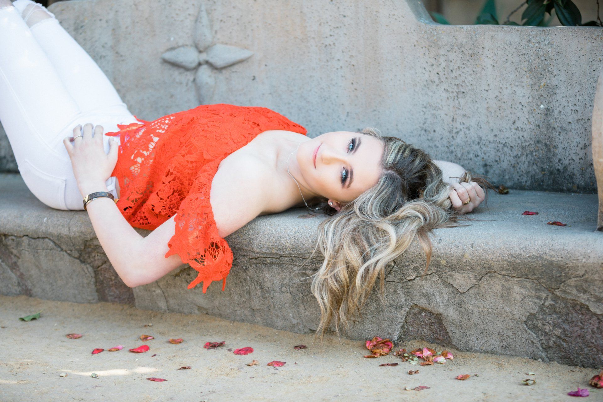 A woman in a red top and white pants is laying on a bench.