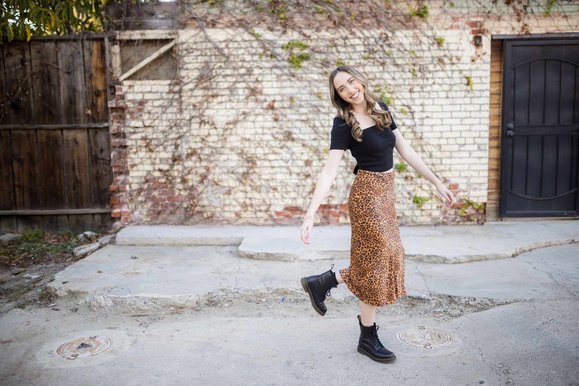 A woman in a leopard print skirt is standing on a sidewalk in front of a brick wall.