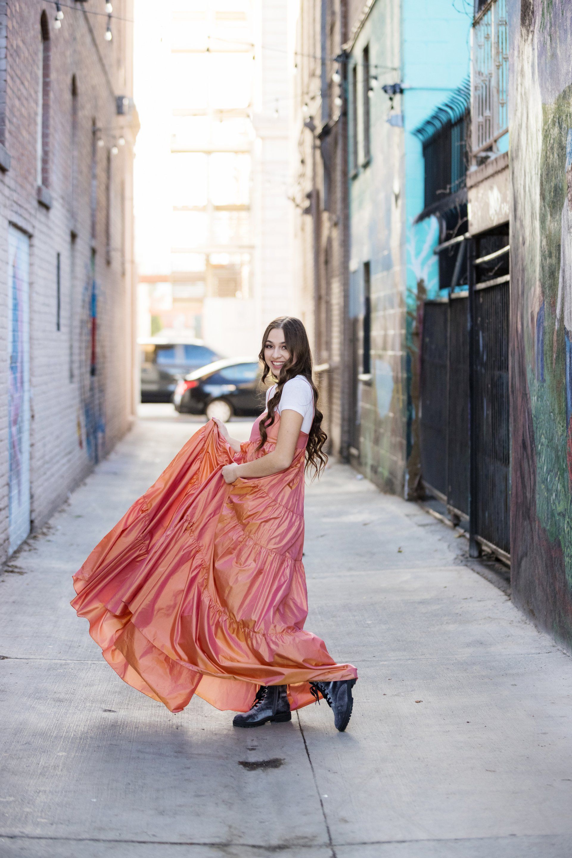 A woman in a long pink dress is dancing in an alleyway.