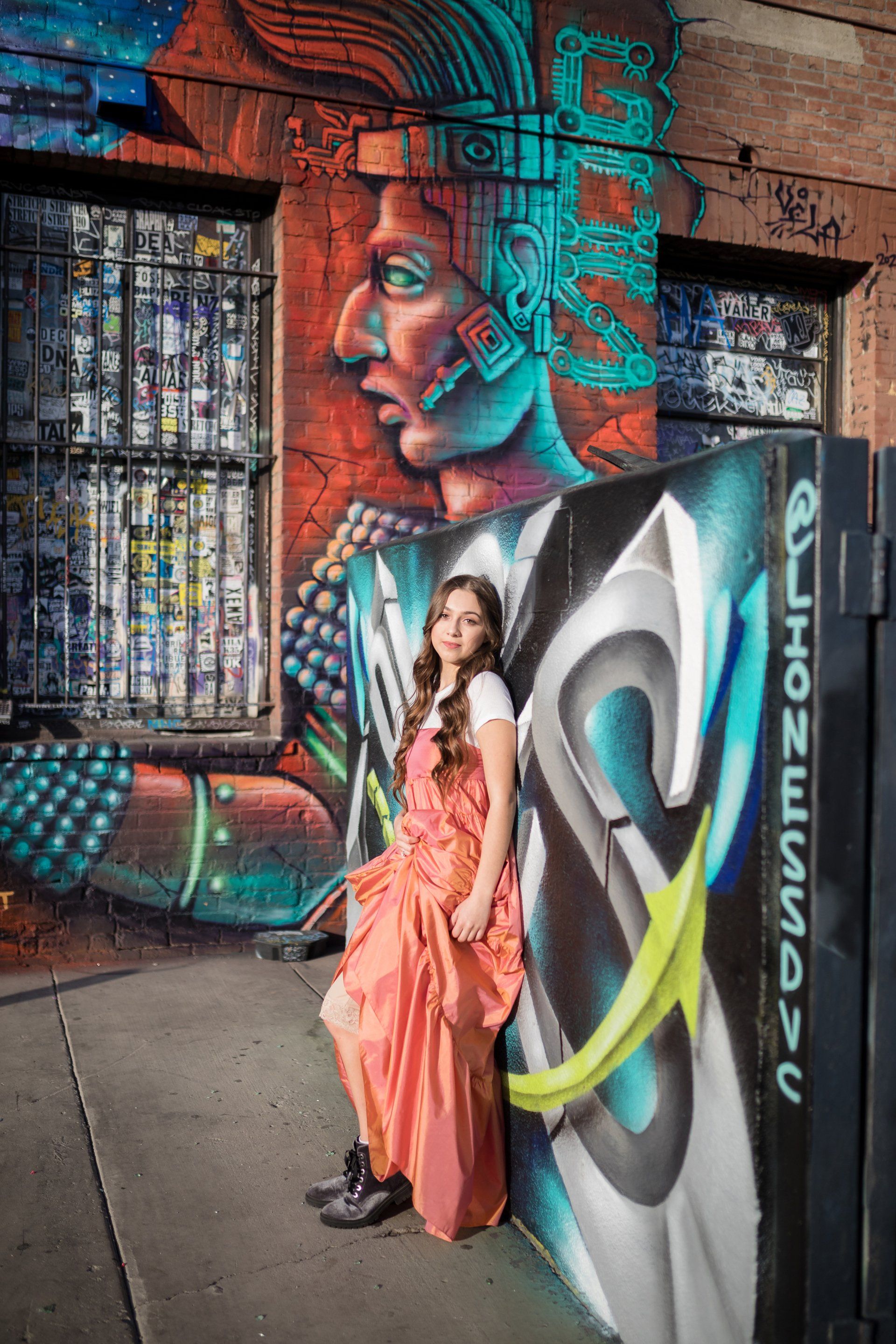 A woman in a long dress is leaning against a wall with graffiti on it.