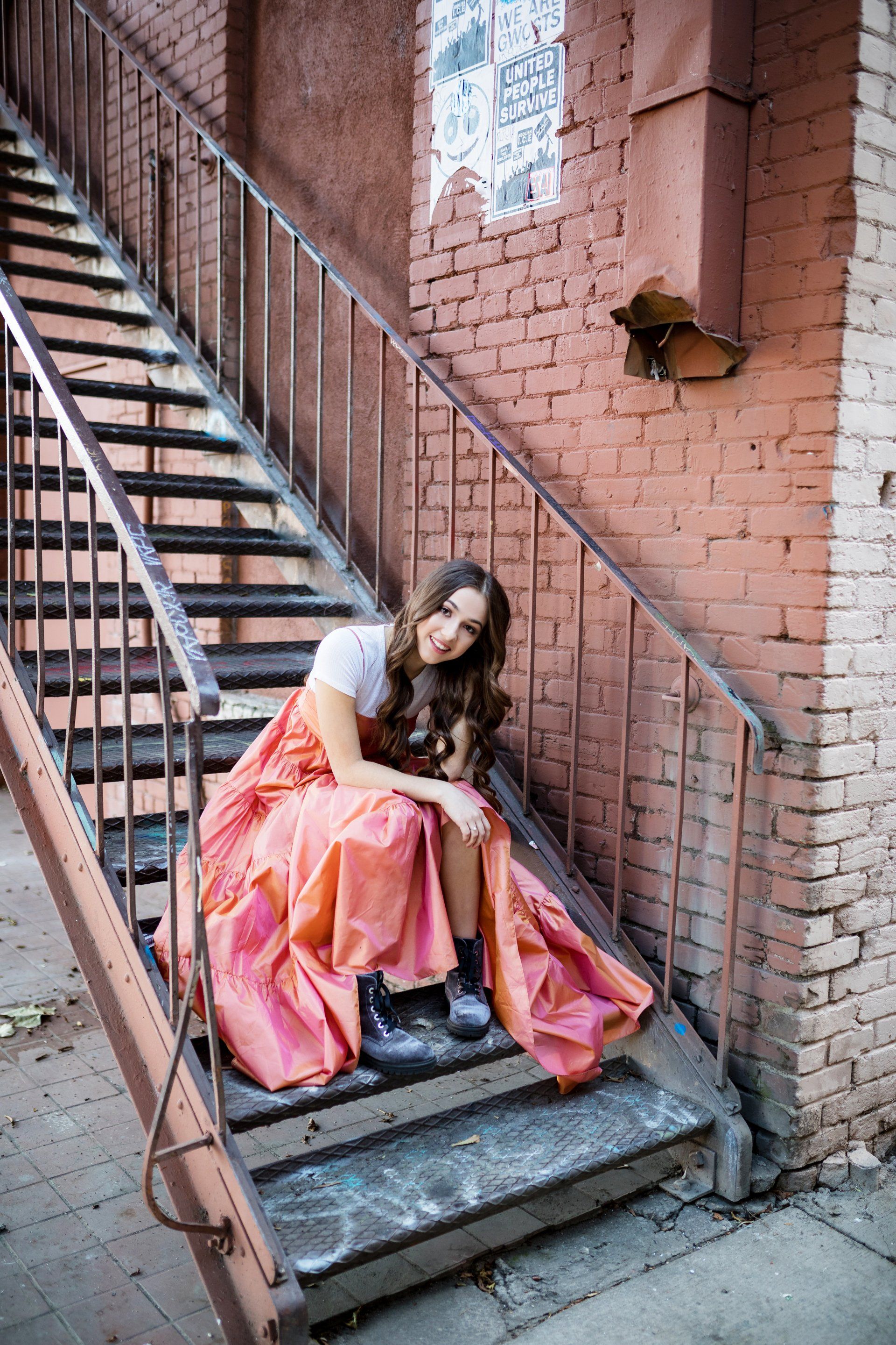 A woman in a long pink dress is sitting on a set of stairs.
