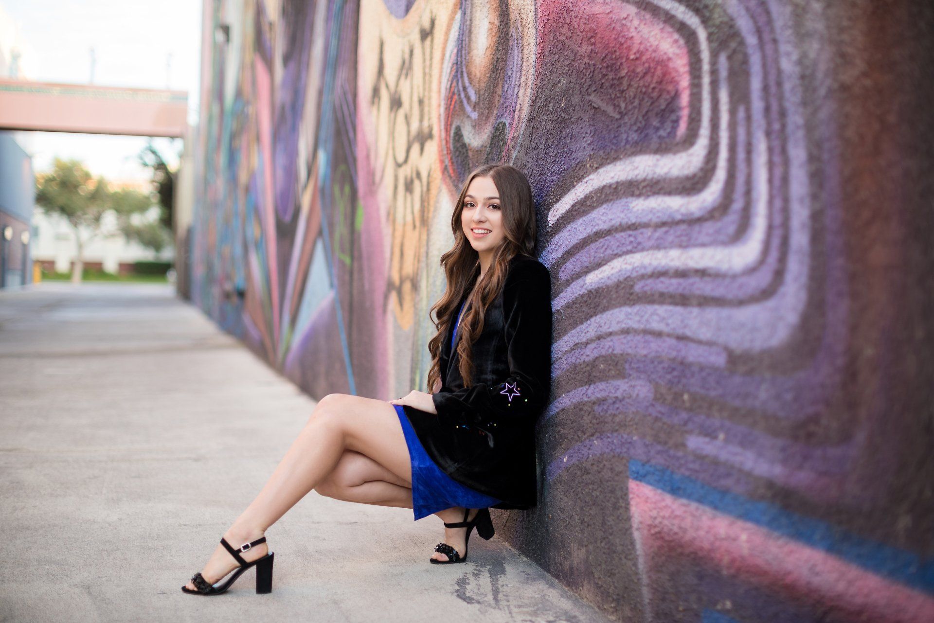 A woman is sitting on the ground in front of a graffiti wall.