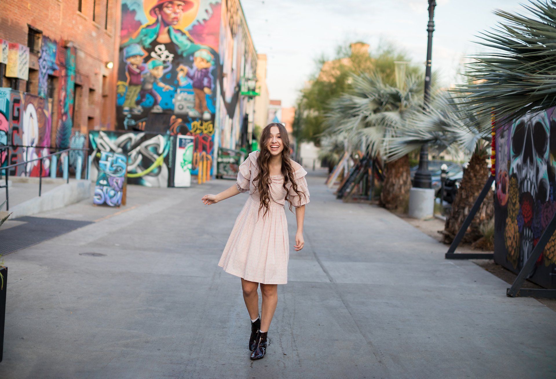 A woman in a pink dress is walking down a street in front of a graffiti wall.