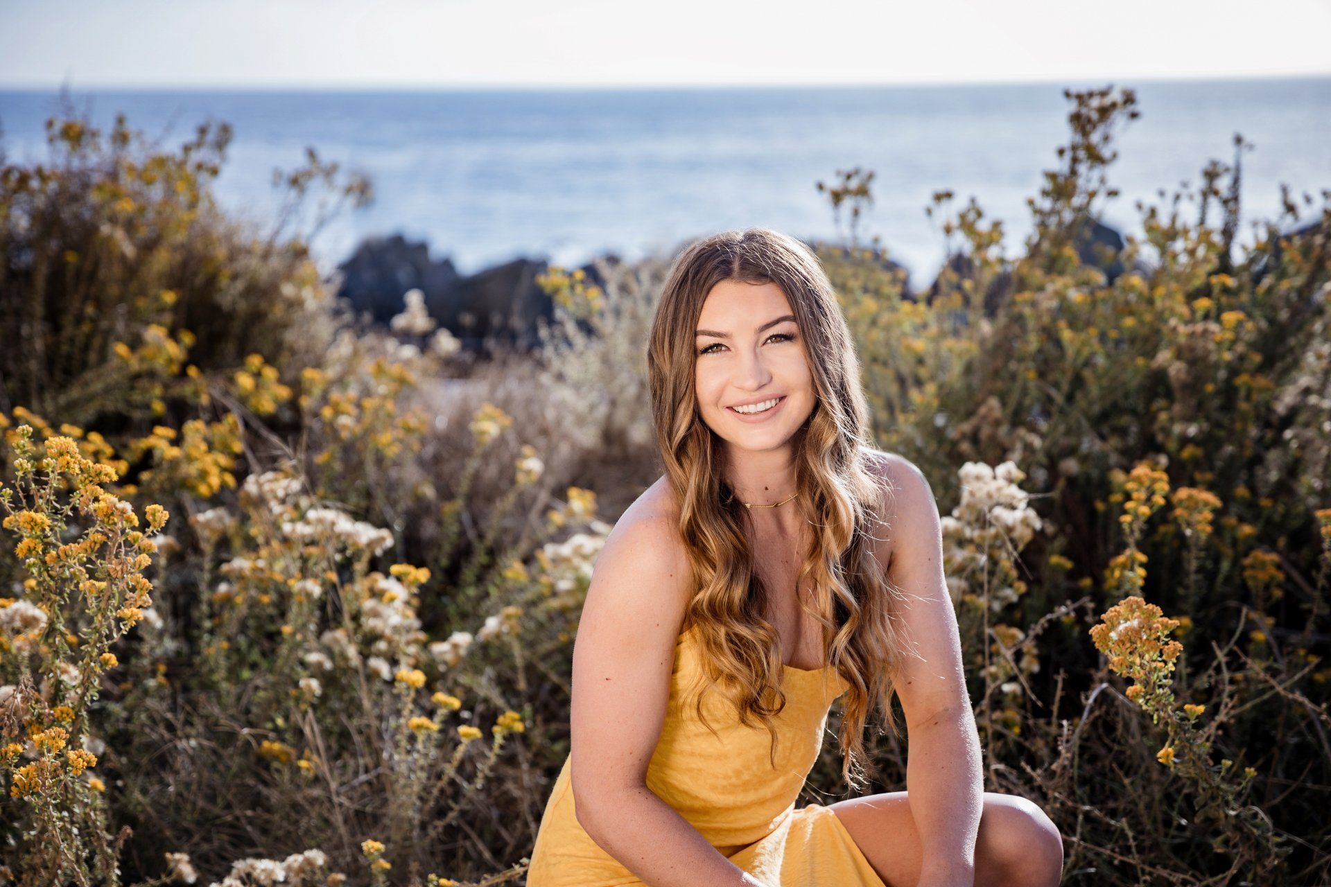 A woman in a yellow dress is sitting in a field of flowers.