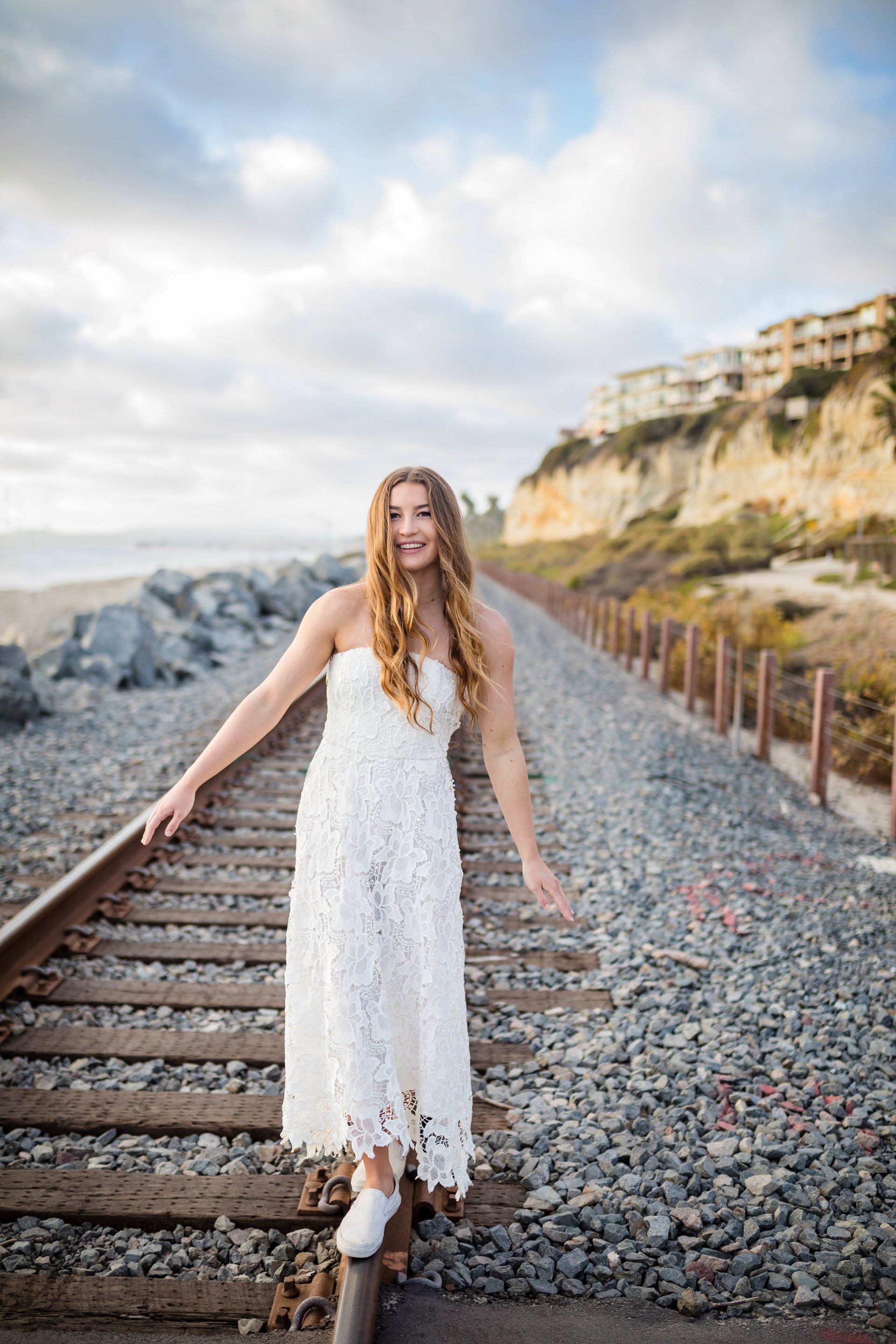 A woman in a white dress is standing on train tracks.