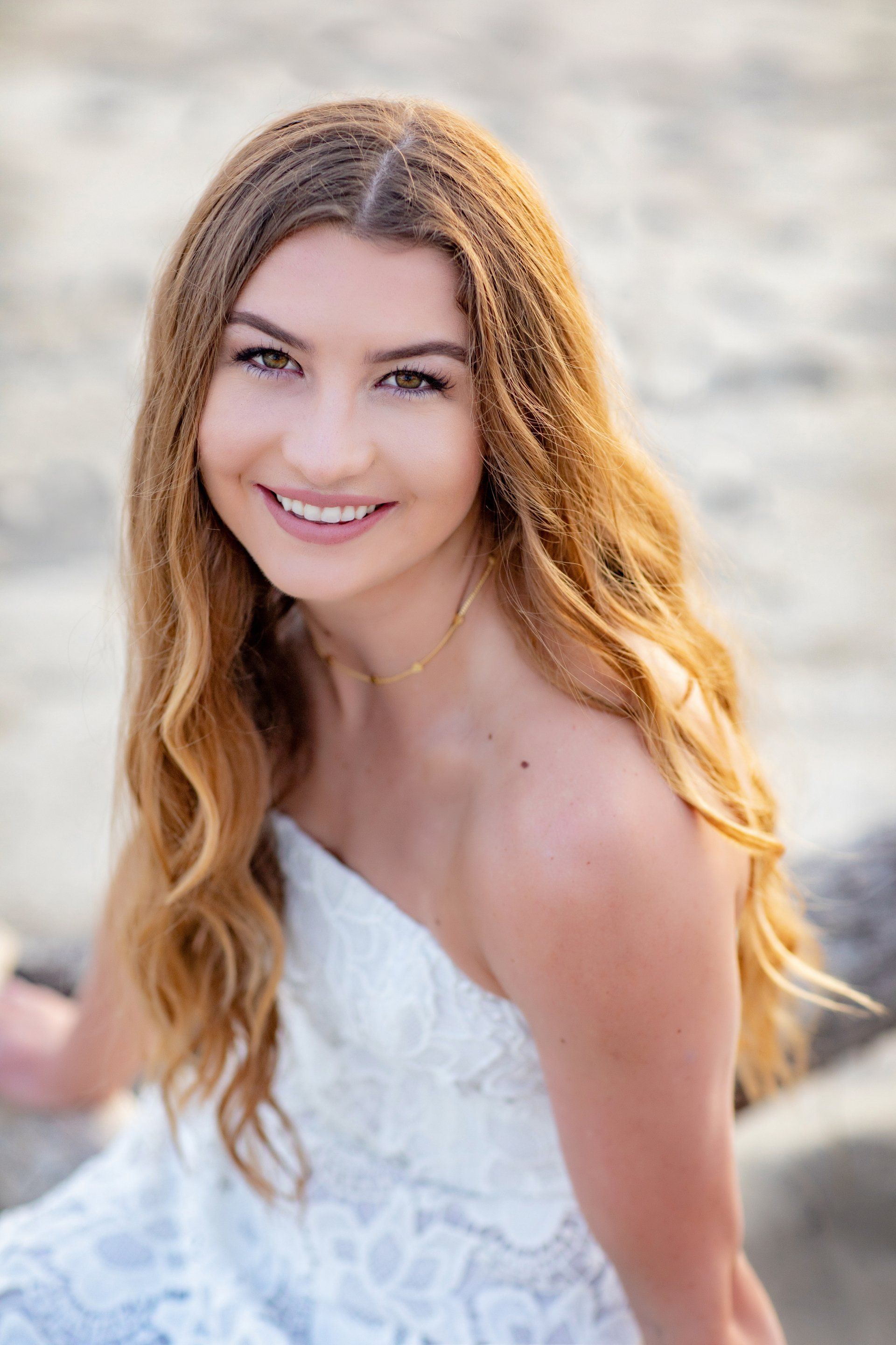 A woman in a white dress is sitting on the beach and smiling.