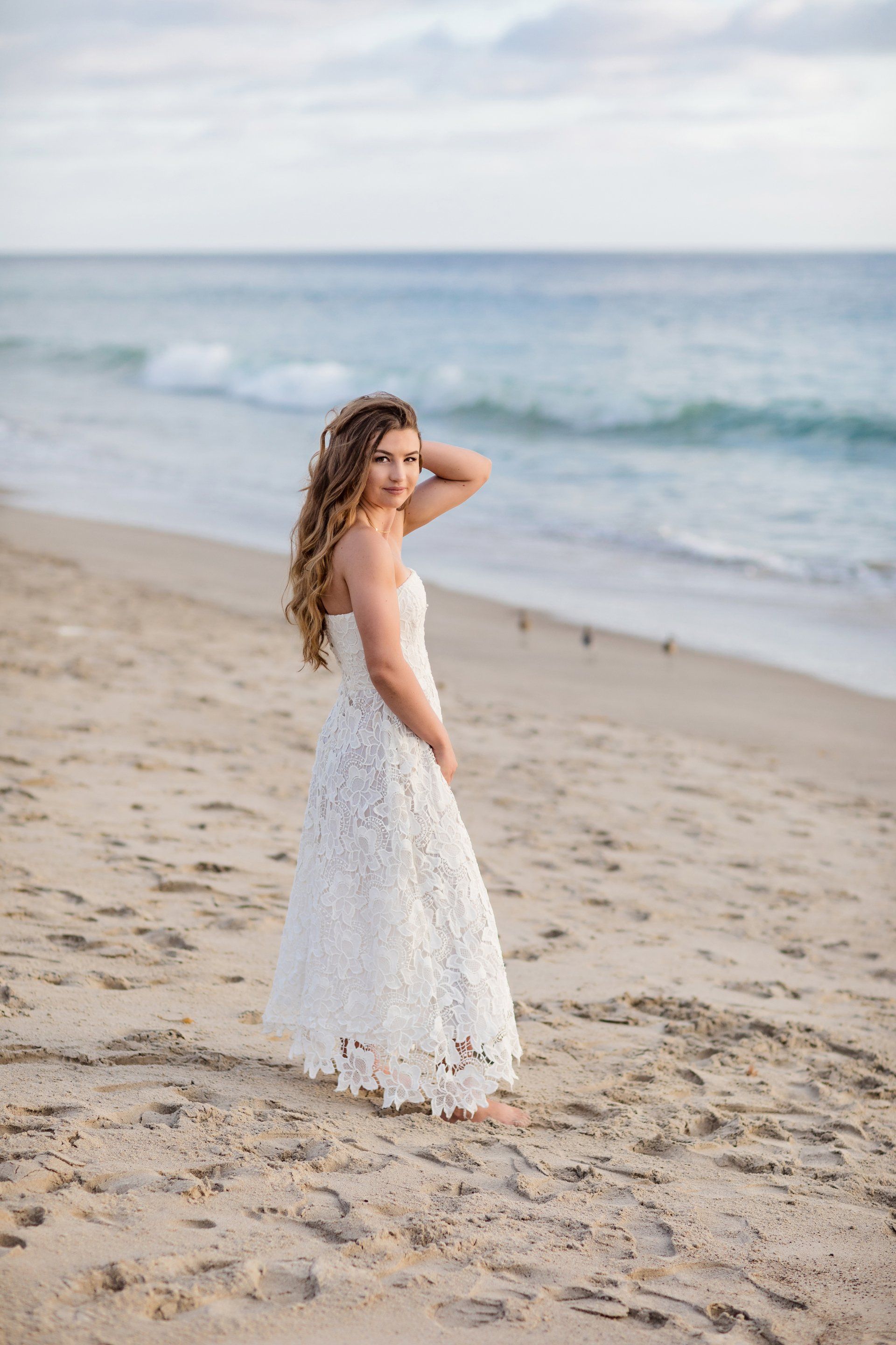 A woman in a white dress is standing on the beach.
